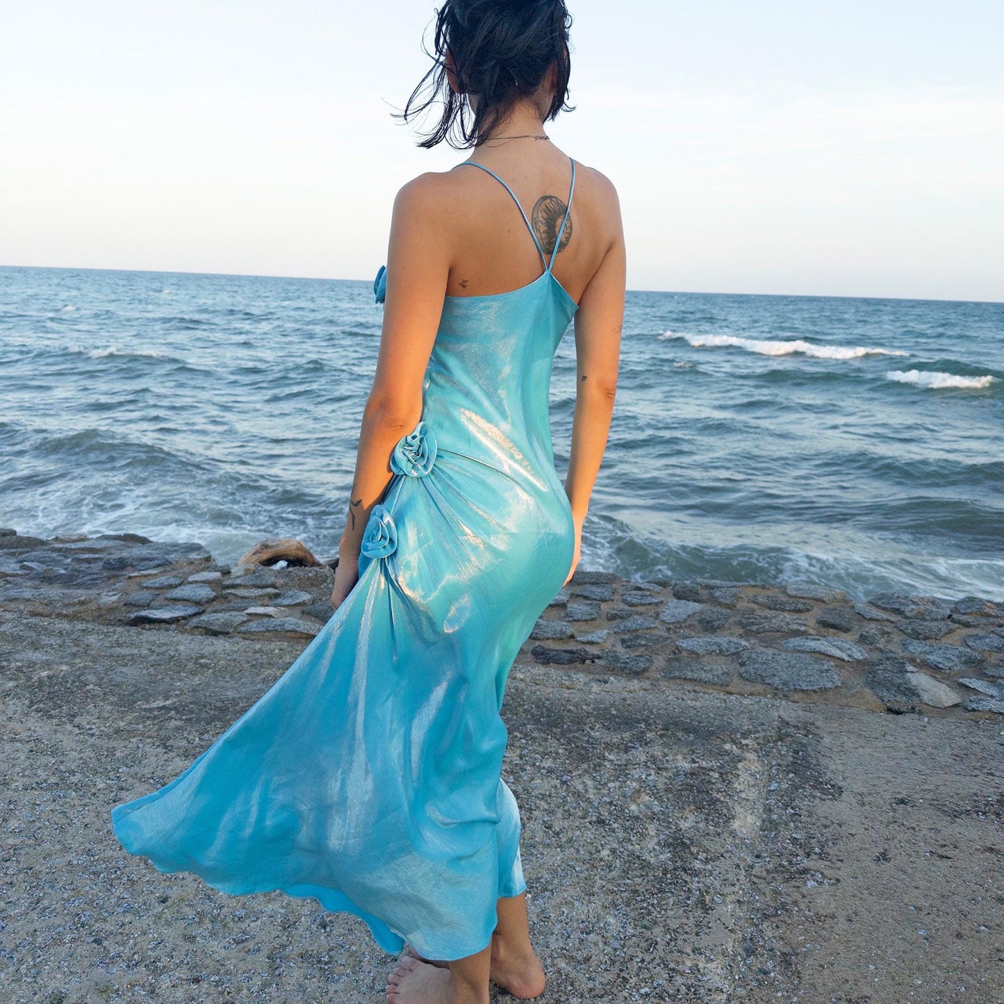 The vintage 2000s blue slip dress is a French-made fantasy with sculptural rosette appliqué along the bust and ruched side detail. Its iridescent finish and fluid midi length evoke a dreamy softness, perfect for proms, summer weddings, or romantic evenings. The silhouette is both delicate and structured, capturing quiet glamour with fairytale allure. A romantic Y2K archive crafted from a shimmering non-stretch fabric. Great vintage condition.