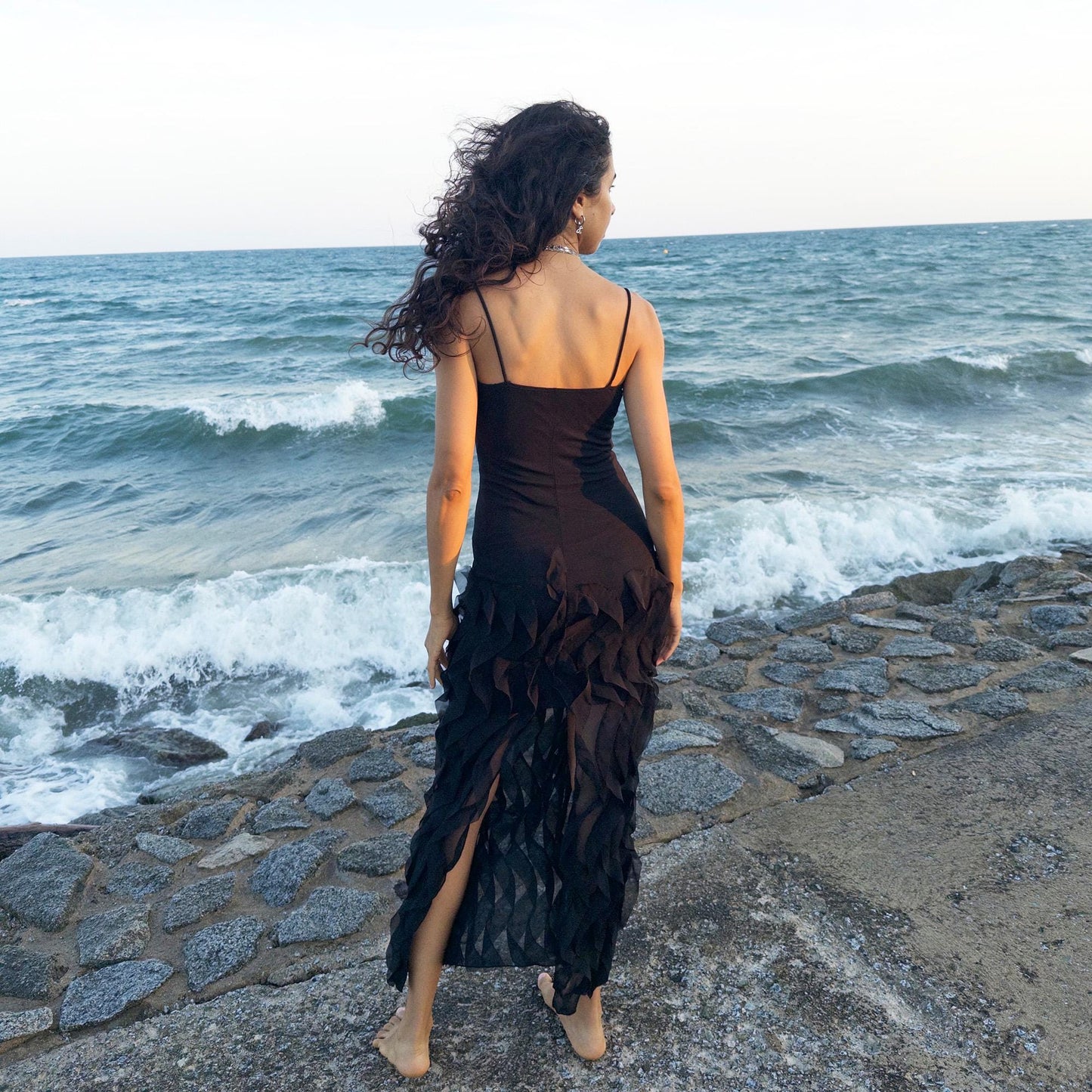 The vintage 90s black mesh midi dress is a sculptural piece with sheer wave appliqué layered across the skirt, minimalist neckline, and a back slit for fluidity. Its body-skimming silhouette fuses quiet sensuality with architectural edge. Ideal for city nights, gallery parties, or modern cocktail looks. An avant garde archive find made in the USA from a stretchy polyester blend. Excellent vintage condition.