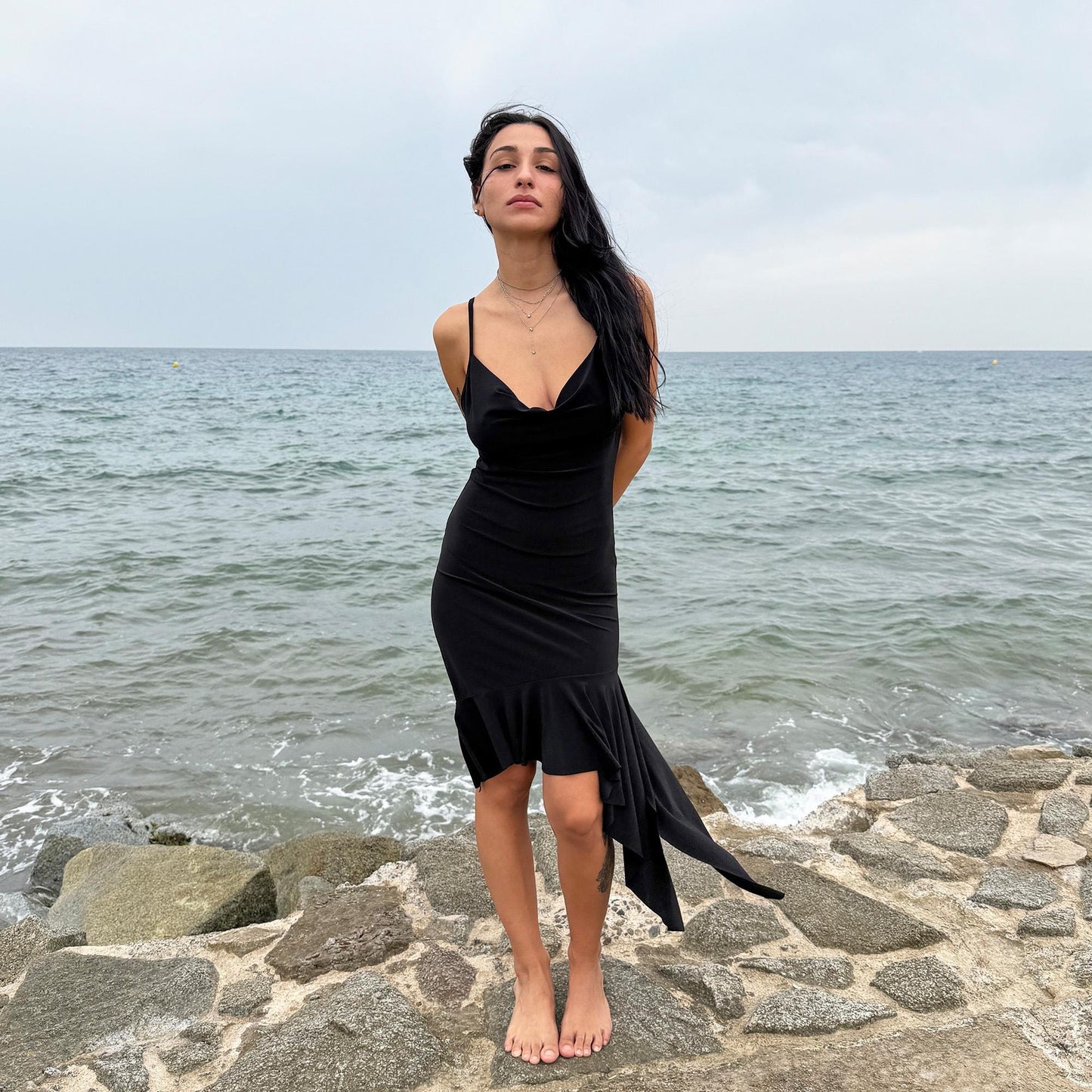This black vintage 2000s dress features a plunging cowl neckline, and an asymmetrical ruffle hem that flutters with movement. Designed in a flattering cocktail length with a body-hugging silhouette, it’s perfect for summer nights, beach parties, or alt club looks. French-made for a dramatic, femme-fatale feel. An iconic Y2K editorial piece for minimalist seduction. Made from a polyester stretch blend. Great vintage condition.