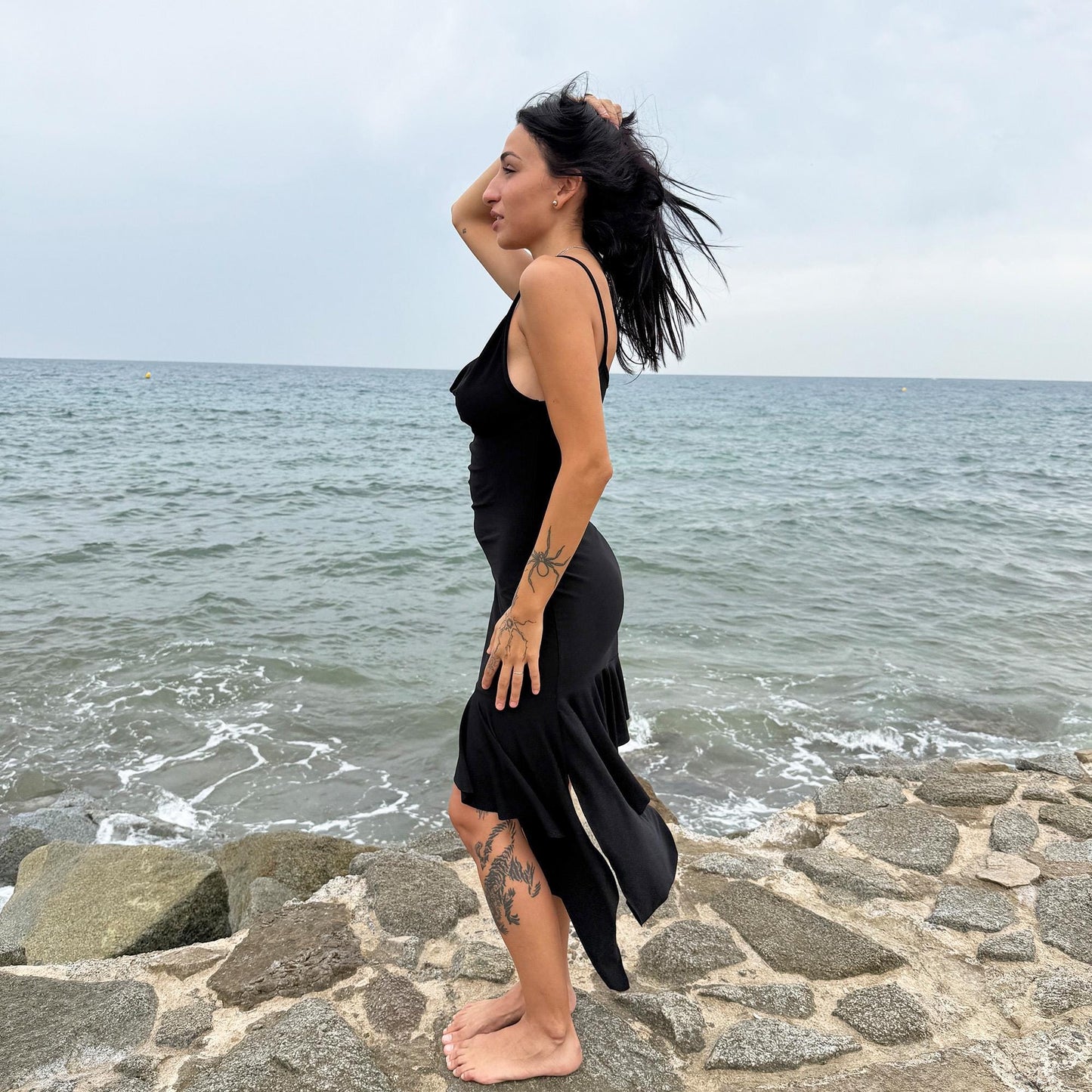 This black vintage 2000s dress features a plunging cowl neckline, and an asymmetrical ruffle hem that flutters with movement. Designed in a flattering cocktail length with a body-hugging silhouette, it’s perfect for summer nights, beach parties, or alt club looks. French-made for a dramatic, femme-fatale feel. An iconic Y2K editorial piece for minimalist seduction. Made from a polyester stretch blend. Great vintage condition.