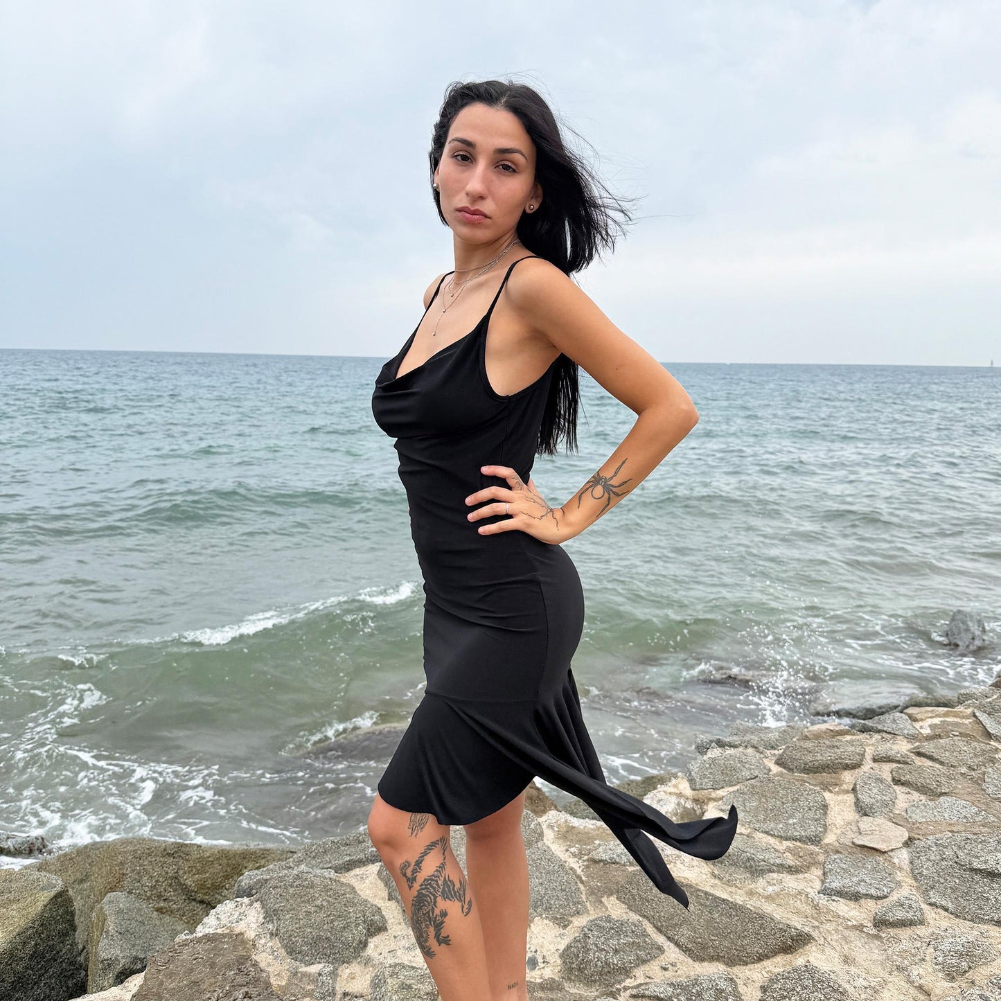 This black vintage 2000s dress features a plunging cowl neckline, and an asymmetrical ruffle hem that flutters with movement. Designed in a flattering cocktail length with a body-hugging silhouette, it’s perfect for summer nights, beach parties, or alt club looks. French-made for a dramatic, femme-fatale feel. An iconic Y2K editorial piece for minimalist seduction. Made from a polyester stretch blend. Great vintage condition.
