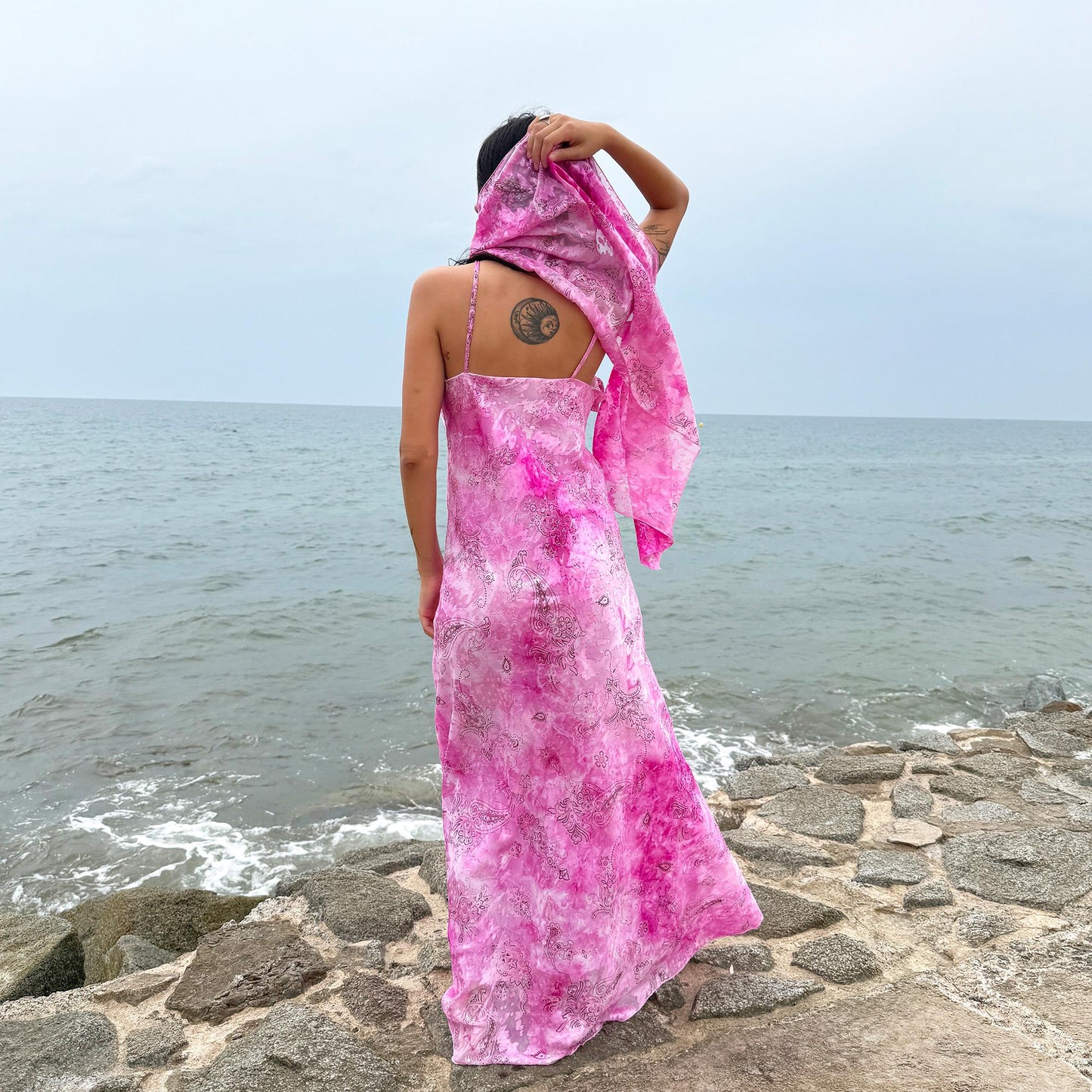 This vintage 2000s slip dress features a vivid pink tie-dye paisley print with rosette appliqué detail at the neckline. It flows into a long silhouette, ideal for summer weddings, proms, or formal parties, and comes with a matching scarf for versatile styling. A romantic archival piece made in France, perfect for bridal, evening, or statement occasions. Made from a non-stretch polyester blend. Excellent vintage condition.