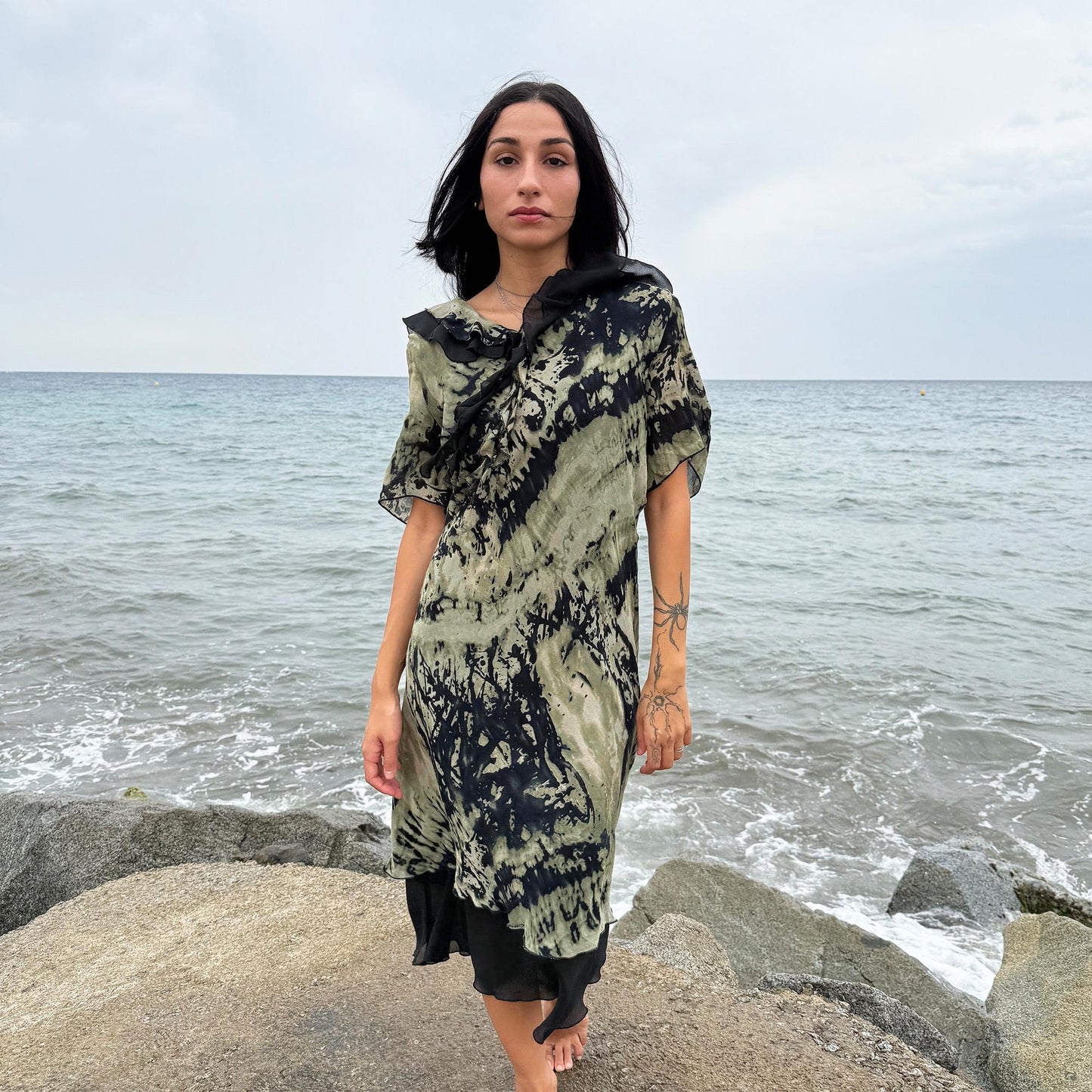 This vintage 90s midi dress features a black and green tie-dye pattern with a ruffled neckline. The short sleeves and flowy layered hem make it ideal for summer festivals, boho gatherings, or dark fairy-inspired looks. A unique Italian-made piece, perfect for forest parties or artistic styling. Made in Italy from lightweight non-stretch fabric. Excellent vintage condition.