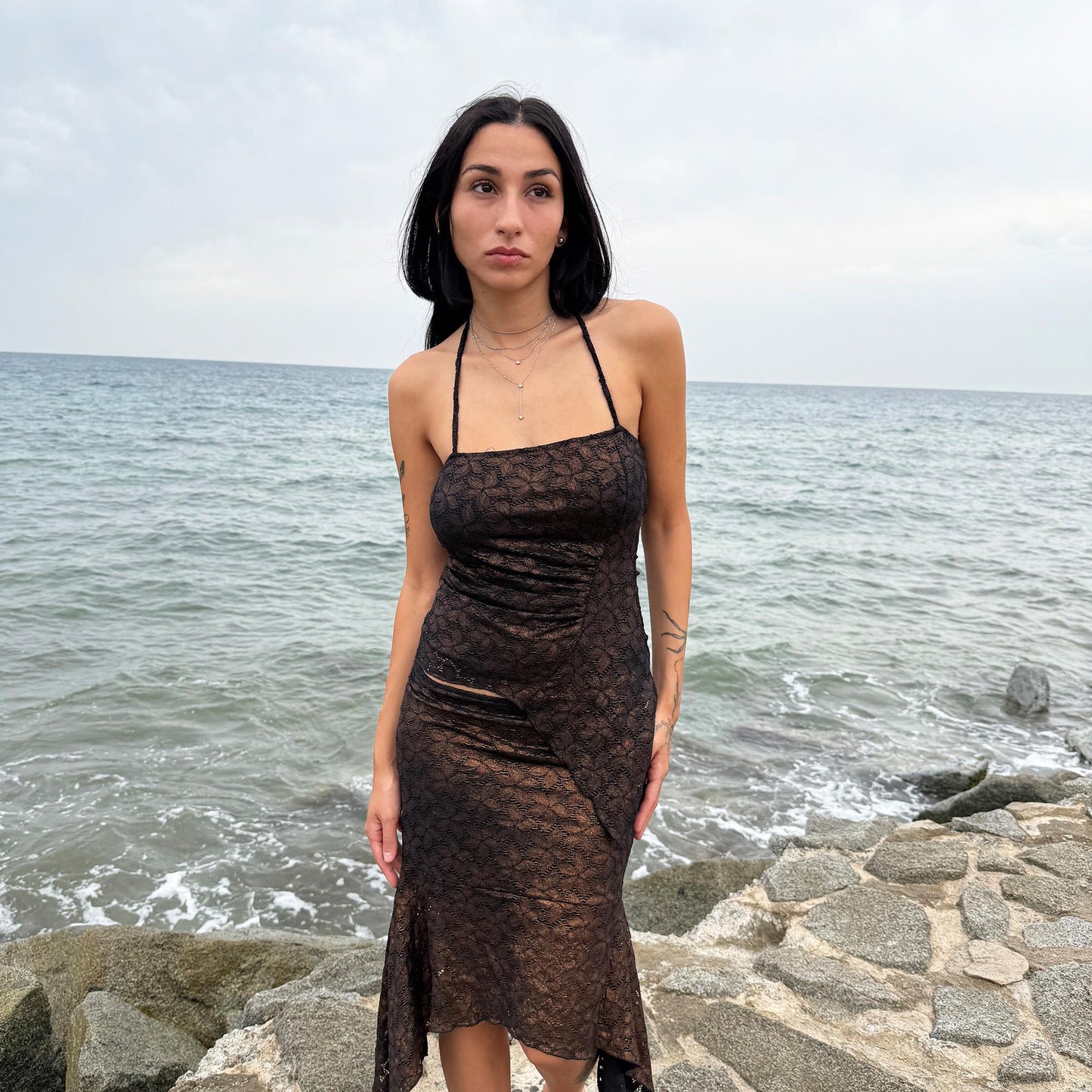 This vintage 2000s two-piece set features a shiny dark bronze-copper and black floral lace pattern. The handkerchief-style asymmetric midi skirt has an elastic waist and is paired with a matching ruched halter tie-neck top with an angled hem. A striking party set, perfect for festivals, summer nights, or dark whimsical styling. A rare archival coord for the ultimate fairy. Made in Spain from a stretchy polyester blend. Excellent vintage condition.