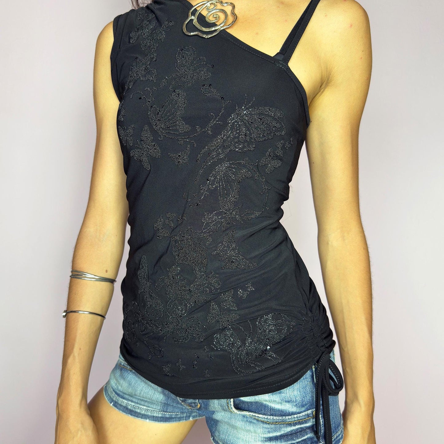 The Y2K Black Sequin Butterfly Top is a vintage 2000s asymmetrical design featuring glittery butterfly motifs, ruched sides, and dual drawstring ties at the shoulder and hem. Crafted from stretchy black fabric with a body-skimming fit, it blends glam detail with subversive edge. Ideal for party nights, clubbing, or iconic festival looks. A millennium-era classic with bold, sculptural energy. Great vintage condition.