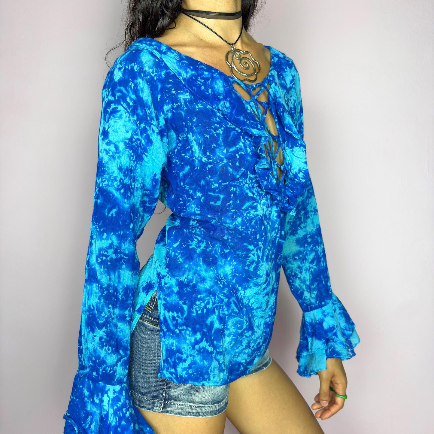 This vintage 90s blue tie dye top features dramatic ruffle cuffs, a deep lace-up neckline, and soft cotton-blend fabric in vibrant psychedelic tones. Designed with long sleeves it channels boho, hippie, and festival energy with bold originality. Lightweight and breathable, perfect for summer layering or statement styling. A rare archival blouse that captures wild 90s freedom. Excellent vintage condition.