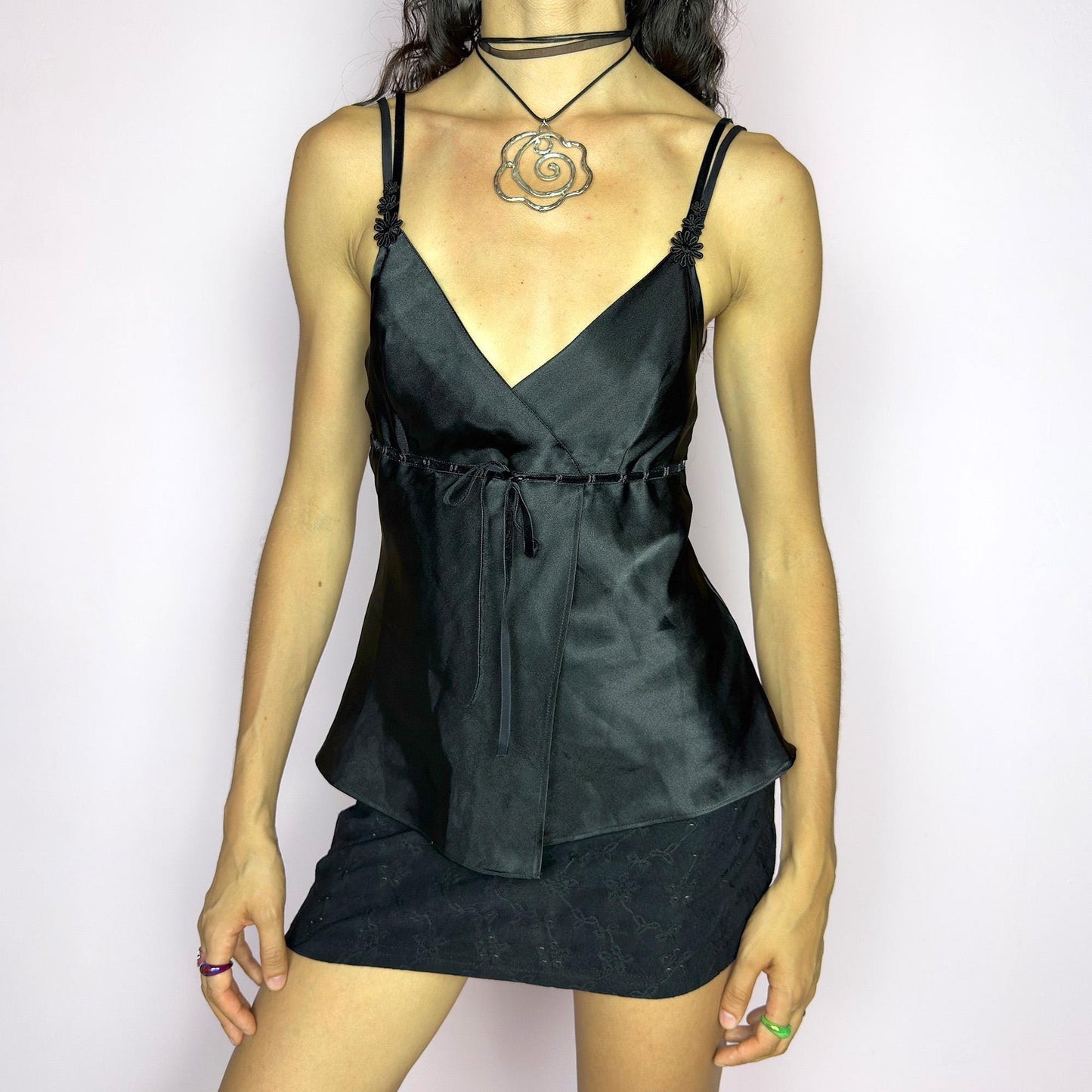 This vintage 90s black satin-style cami top features a wrap front silhouette with a subtle tie at the waist, adding gentle structure to its soft drape. Finished with delicate floral appliqués and adjustable double spaghetti straps, it captures a mood of refined sensuality. Perfect for cocktail nights, evening events, or romantic layering. Lightweight and fluid, it brings feminine elegance with a hint of 90s glamour. Excellent vintage condition.