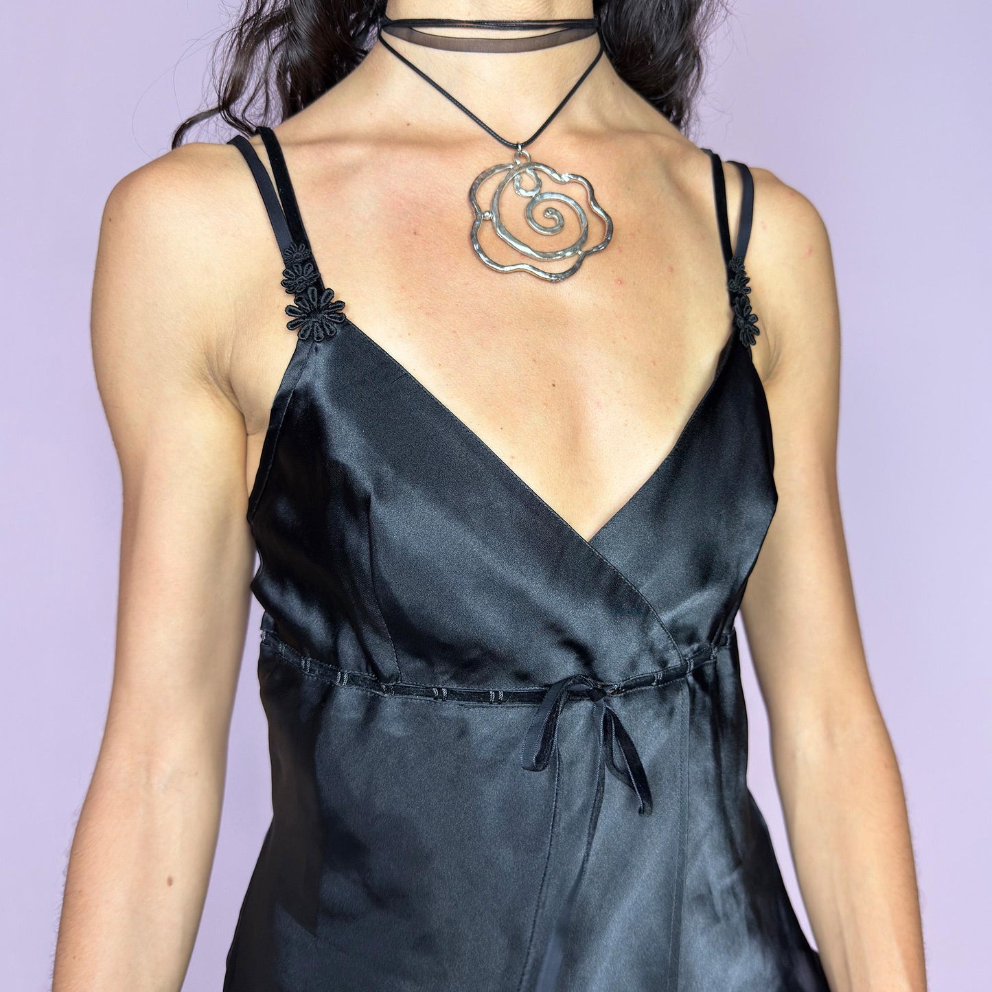 This vintage 90s black satin-style cami top features a wrap front silhouette with a subtle tie at the waist, adding gentle structure to its soft drape. Finished with delicate floral appliqués and adjustable double spaghetti straps, it captures a mood of refined sensuality. Perfect for cocktail nights, evening events, or romantic layering. Lightweight and fluid, it brings feminine elegance with a hint of 90s glamour. Excellent vintage condition.