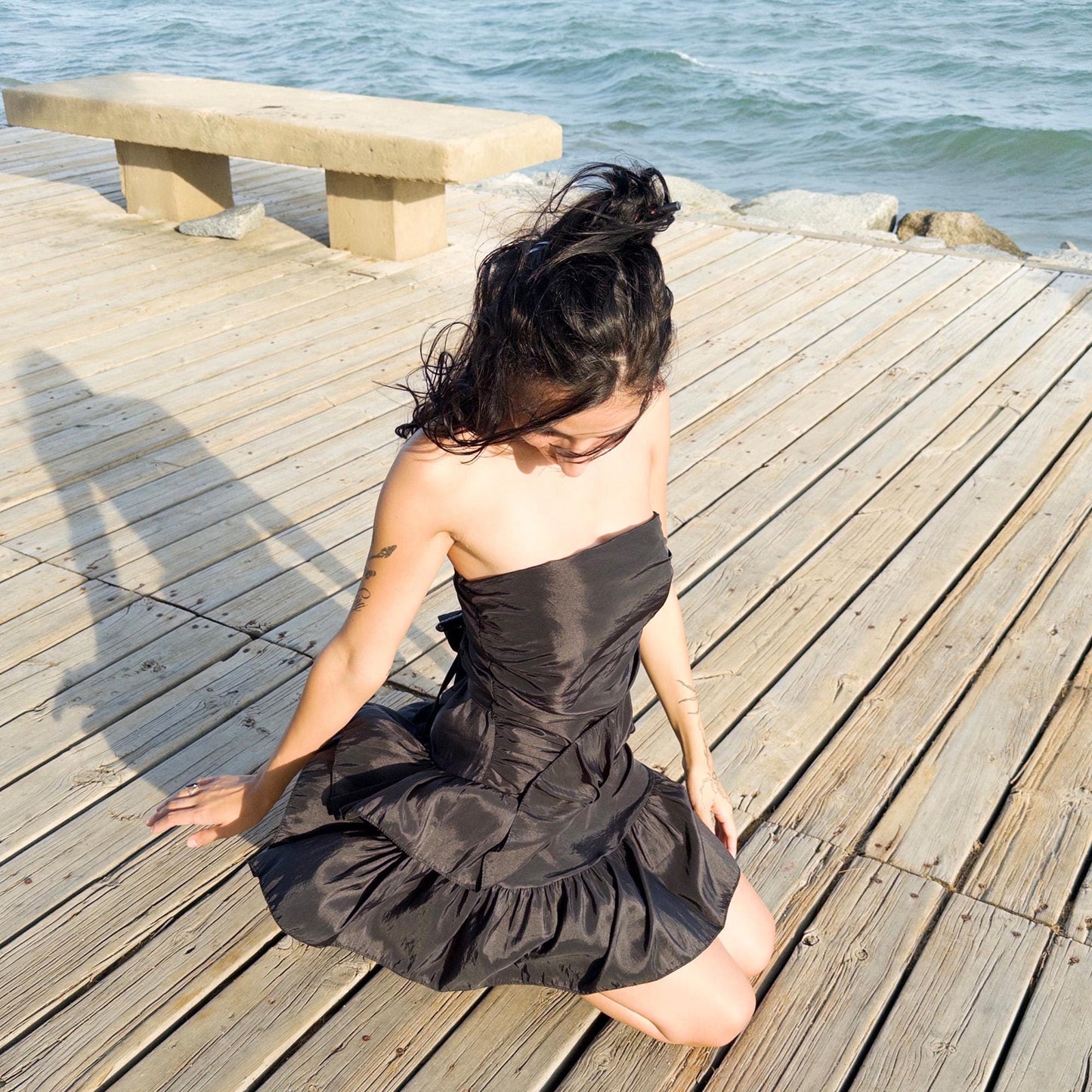 The vintage 90s black mini dress is a sculptural, strapless piece with ruched draping and voluminous double ruffle tiers. Made in Italy, it features a tie-back sash, shirred elastic panel, and side zip for a secure, flattering fit. Crafted from a polyester blend, it catches light effortlessly—ideal for summer nights, cocktail events, or rooftop parties. A super cute dress with high femme drama. Excellent vintage condition.
