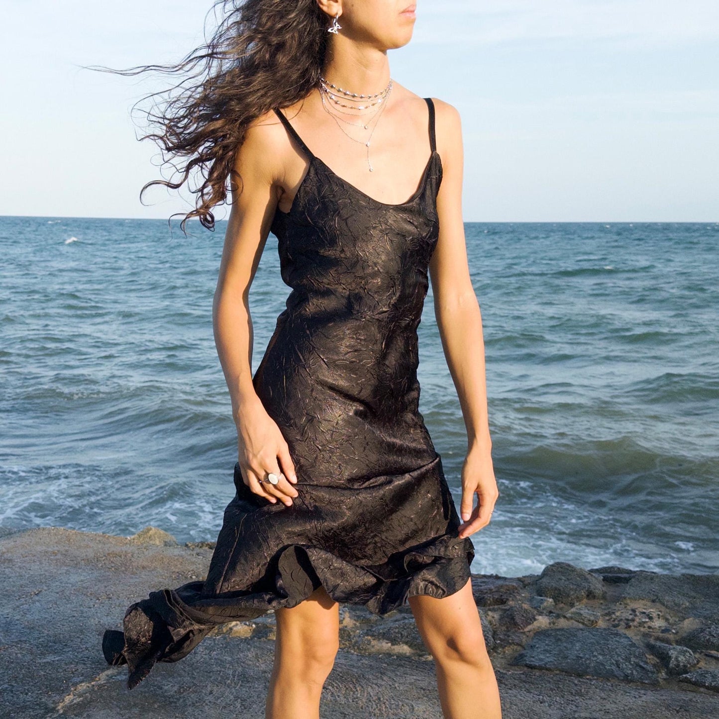 The vintage 2000s black slip dress is a made-in-France piece with crinkled texture and asymmetric ruffle hem. Its sculptural midi silhouette moves with quiet sensuality—ideal for gallery openings, formal nights, or late summer dates. A deconstructed Y2K shape that evokes avant-garde elegance, made to be seen without shouting. An archival dress crafted from a soft polyester blend. Excellent vintage condition.