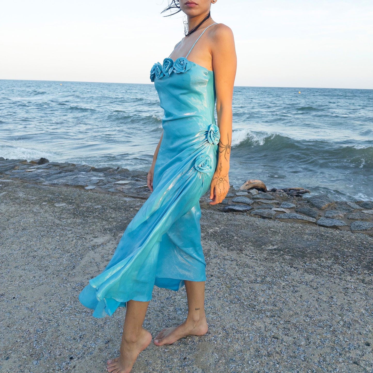 The vintage 2000s blue slip dress is a French-made fantasy with sculptural rosette appliqué along the bust and ruched side detail. Its iridescent finish and fluid midi length evoke a dreamy softness, perfect for proms, summer weddings, or romantic evenings. The silhouette is both delicate and structured, capturing quiet glamour with fairytale allure. A romantic Y2K archive crafted from a shimmering non-stretch fabric. Great vintage condition.