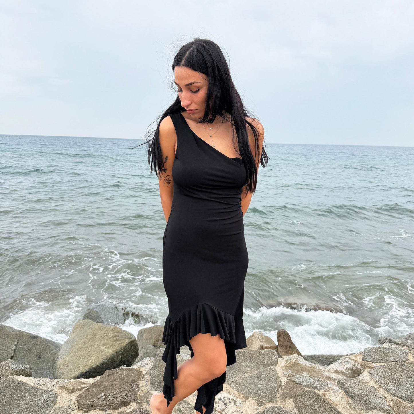 This vintage 2000s black mini dress features asymmetric straps with a subtle cowl neckline and a dramatic ruffled hem. Crafted from a stretchy fabric, it flatters the body with a bold party silhouette. Perfect for summer nights, club looks, or diva-inspired Y2K styling, this piece captures iconic 2000s glamour. Excellent vintage condition.