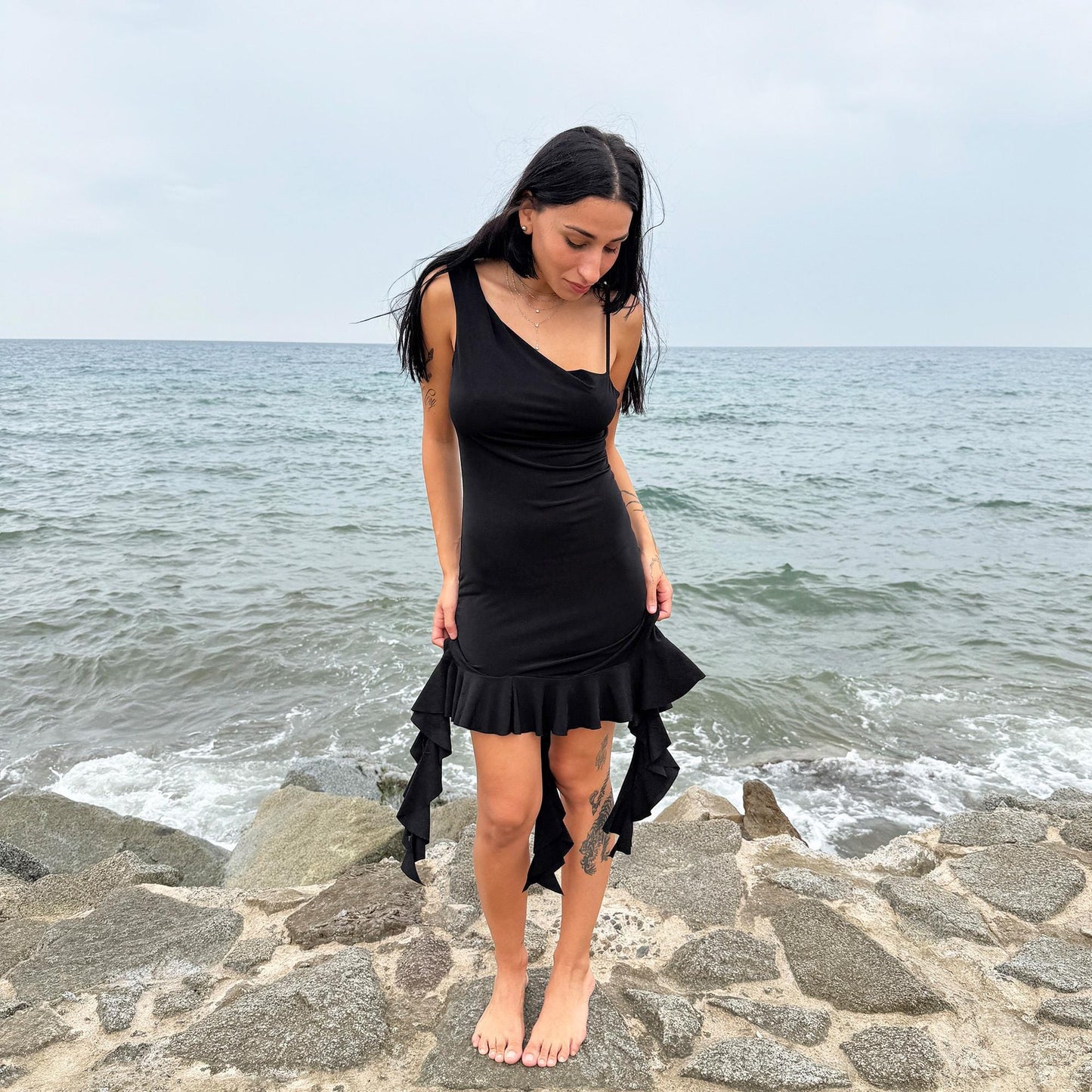 This vintage 2000s black mini dress features asymmetric straps with a subtle cowl neckline and a dramatic ruffled hem. Crafted from a stretchy fabric, it flatters the body with a bold party silhouette. Perfect for summer nights, club looks, or diva-inspired Y2K styling, this piece captures iconic 2000s glamour. Excellent vintage condition.