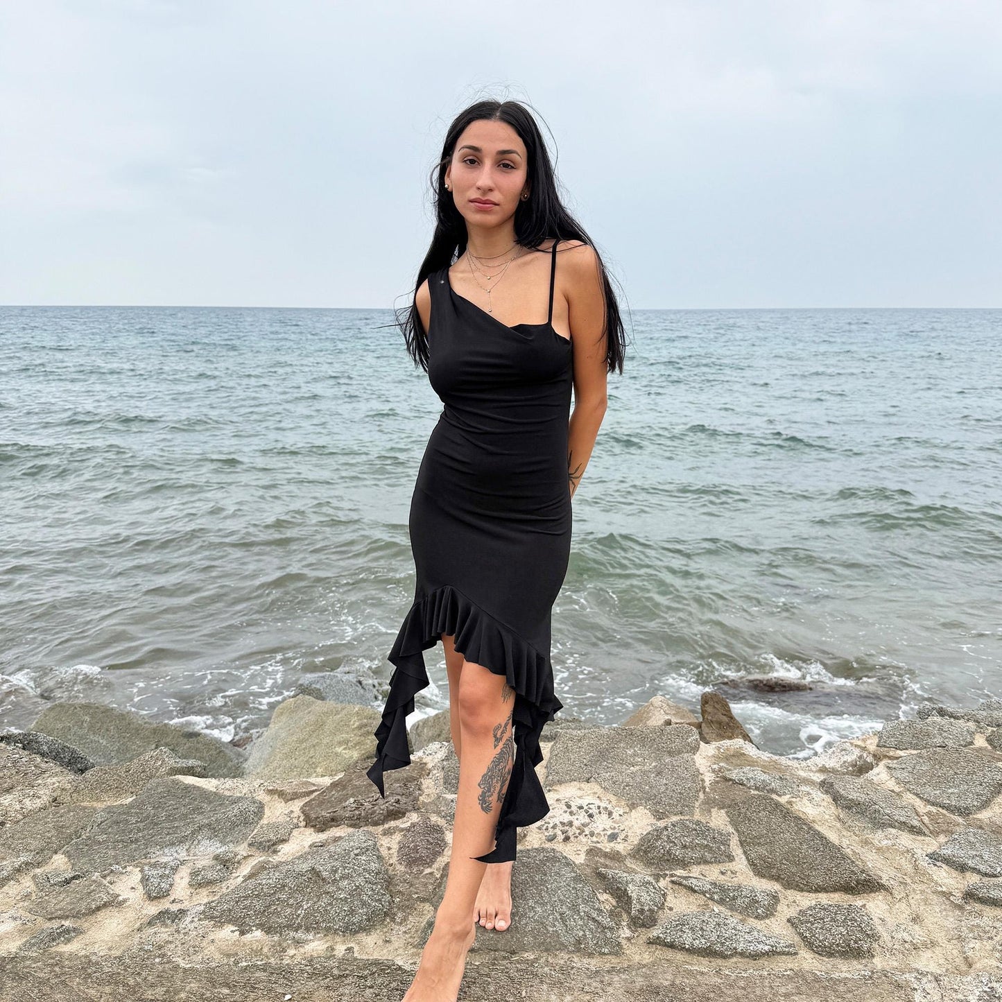 This vintage 2000s black mini dress features asymmetric straps with a subtle cowl neckline and a dramatic ruffled hem. Crafted from a stretchy fabric, it flatters the body with a bold party silhouette. Perfect for summer nights, club looks, or diva-inspired Y2K styling, this piece captures iconic 2000s glamour. Excellent vintage condition.