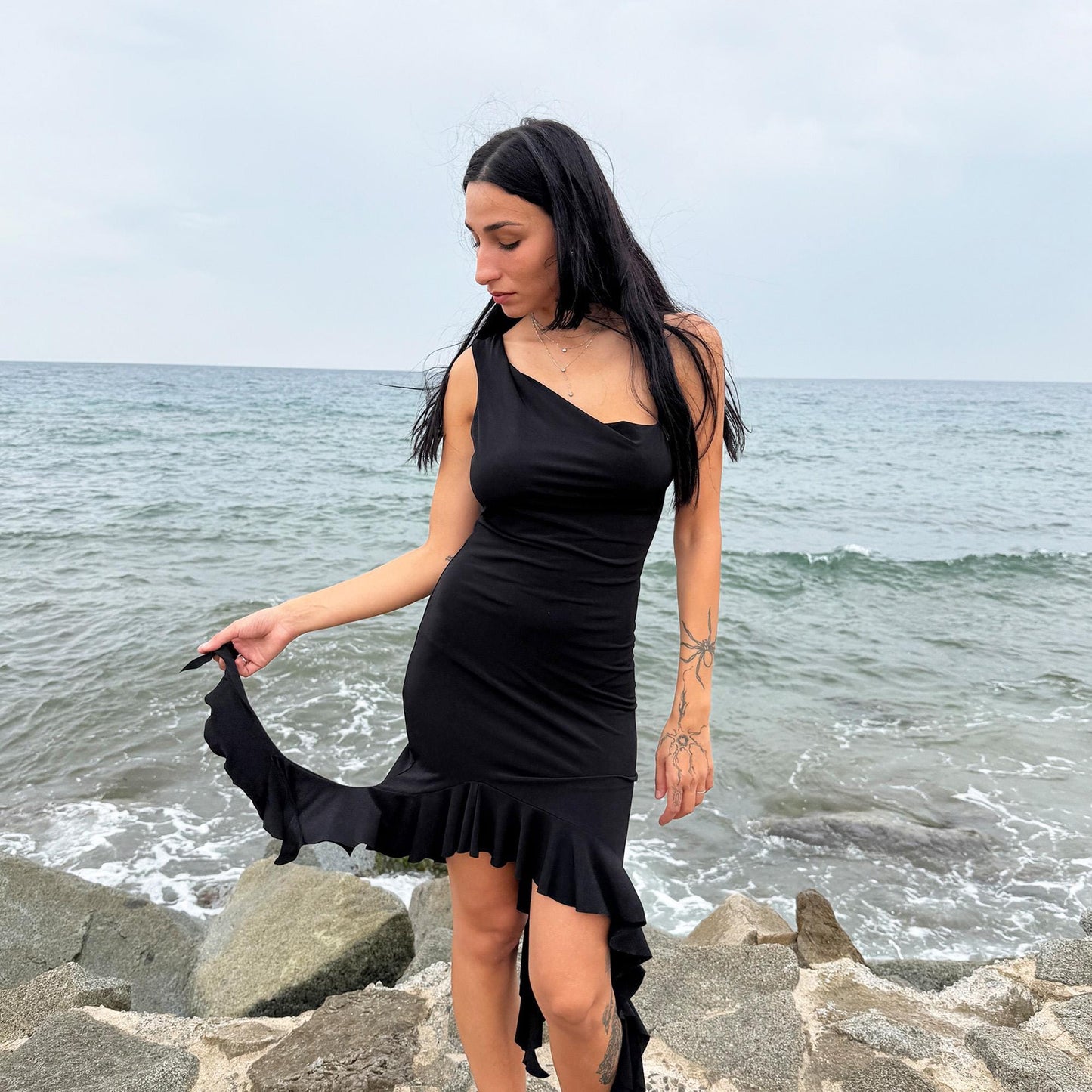 This vintage 2000s black mini dress features asymmetric straps with a subtle cowl neckline and a dramatic ruffled hem. Crafted from a stretchy fabric, it flatters the body with a bold party silhouette. Perfect for summer nights, club looks, or diva-inspired Y2K styling, this piece captures iconic 2000s glamour. Excellent vintage condition.