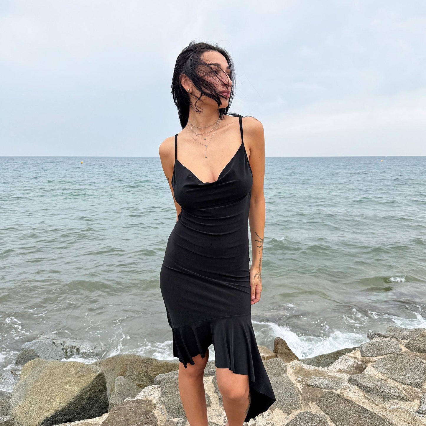 This black vintage 2000s dress features a plunging cowl neckline, and an asymmetrical ruffle hem that flutters with movement. Designed in a flattering cocktail length with a body-hugging silhouette, it’s perfect for summer nights, beach parties, or alt club looks. French-made for a dramatic, femme-fatale feel. An iconic Y2K editorial piece for minimalist seduction. Made from a polyester stretch blend. Great vintage condition.