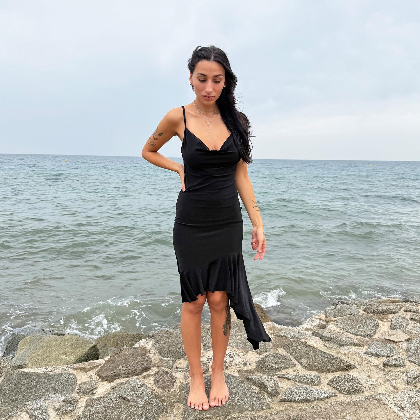 This black vintage 2000s dress features a plunging cowl neckline, and an asymmetrical ruffle hem that flutters with movement. Designed in a flattering cocktail length with a body-hugging silhouette, it’s perfect for summer nights, beach parties, or alt club looks. French-made for a dramatic, femme-fatale feel. An iconic Y2K editorial piece for minimalist seduction. Made from a polyester stretch blend. Great vintage condition.