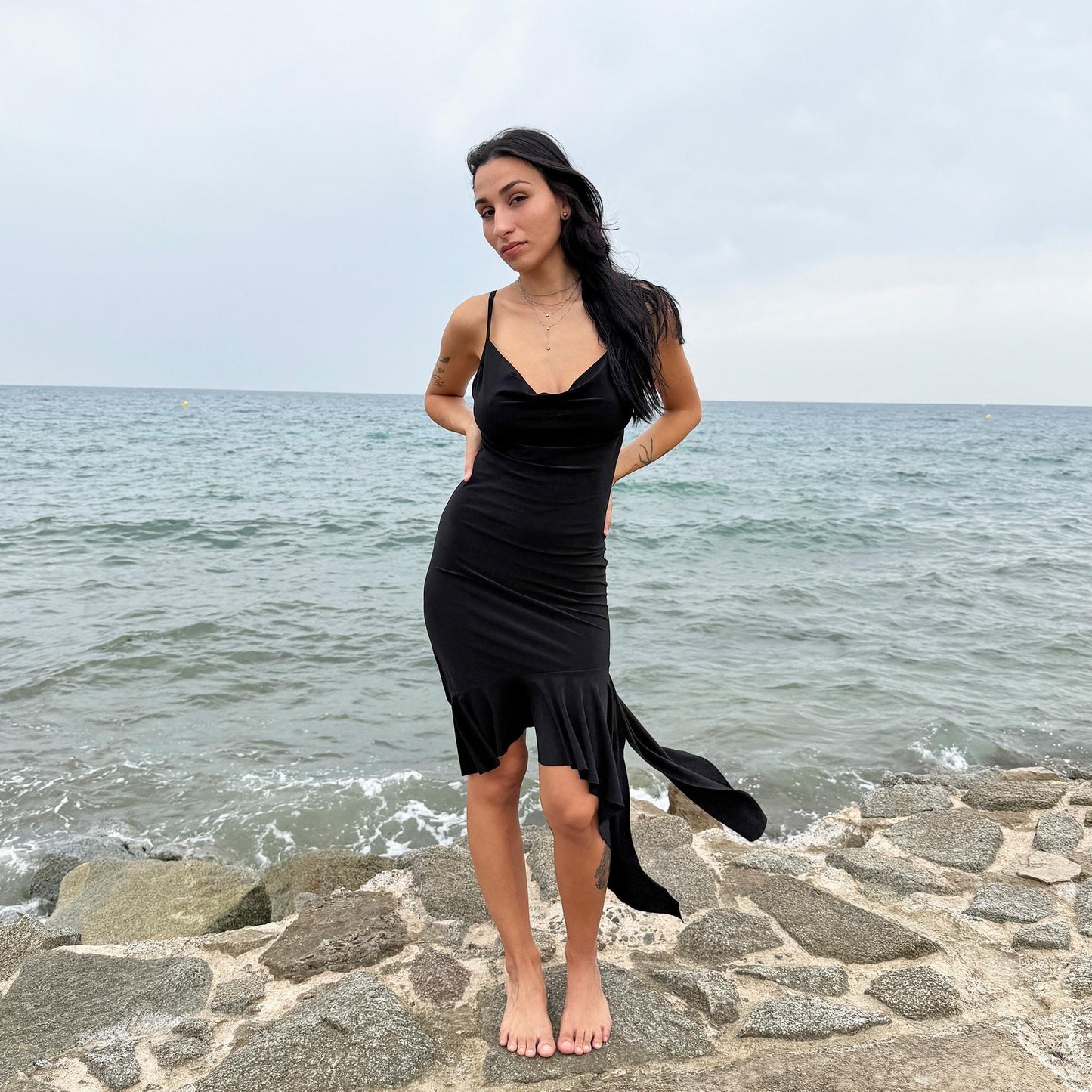 This black vintage 2000s dress features a plunging cowl neckline, and an asymmetrical ruffle hem that flutters with movement. Designed in a flattering cocktail length with a body-hugging silhouette, it’s perfect for summer nights, beach parties, or alt club looks. French-made for a dramatic, femme-fatale feel. An iconic Y2K editorial piece for minimalist seduction. Made from a polyester stretch blend. Great vintage condition.