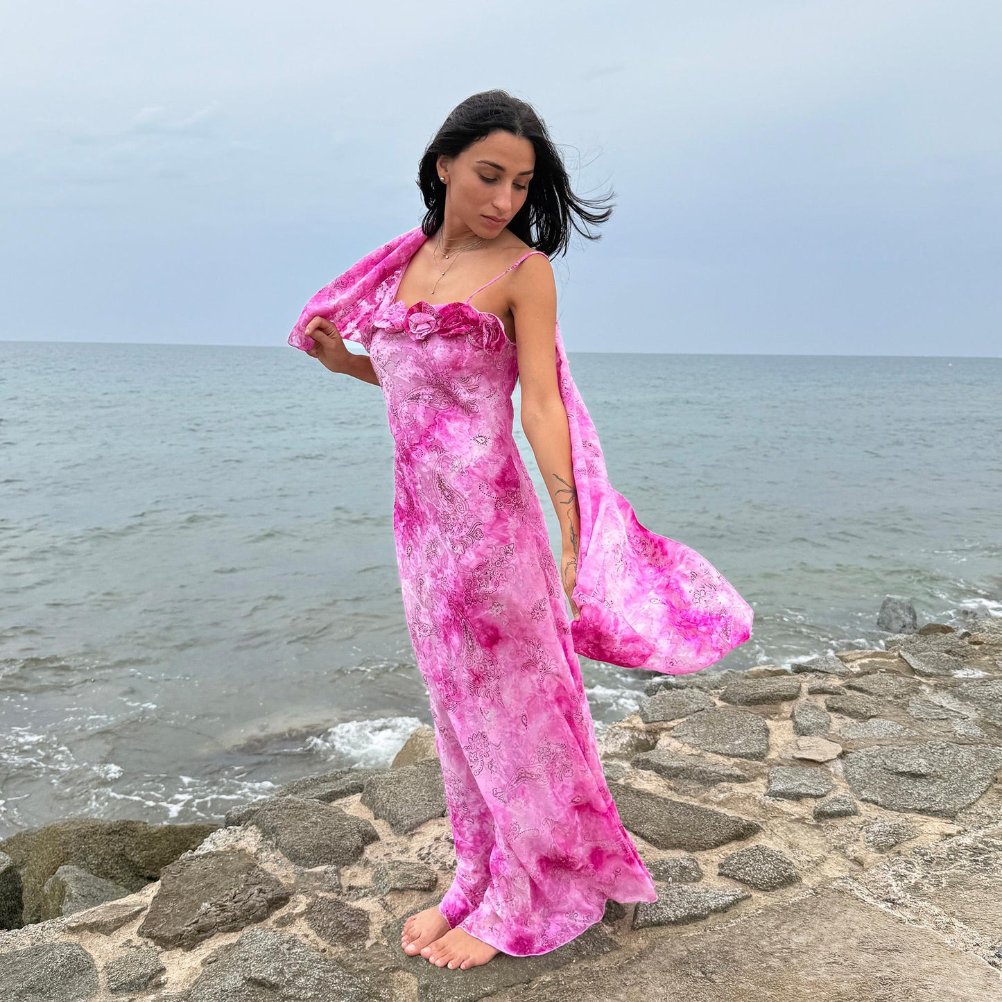 This vintage 2000s slip dress features a vivid pink tie-dye paisley print with rosette appliqué detail at the neckline. It flows into a long silhouette, ideal for summer weddings, proms, or formal parties, and comes with a matching scarf for versatile styling. A romantic archival piece made in France, perfect for bridal, evening, or statement occasions. Made from a non-stretch polyester blend. Excellent vintage condition.