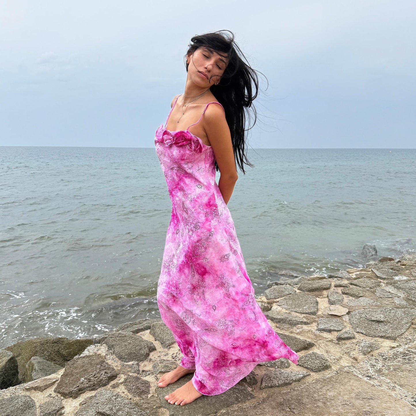 This vintage 2000s slip dress features a vivid pink tie-dye paisley print with rosette appliqué detail at the neckline. It flows into a long silhouette, ideal for summer weddings, proms, or formal parties, and comes with a matching scarf for versatile styling. A romantic archival piece made in France, perfect for bridal, evening, or statement occasions. Made from a non-stretch polyester blend. Excellent vintage condition.