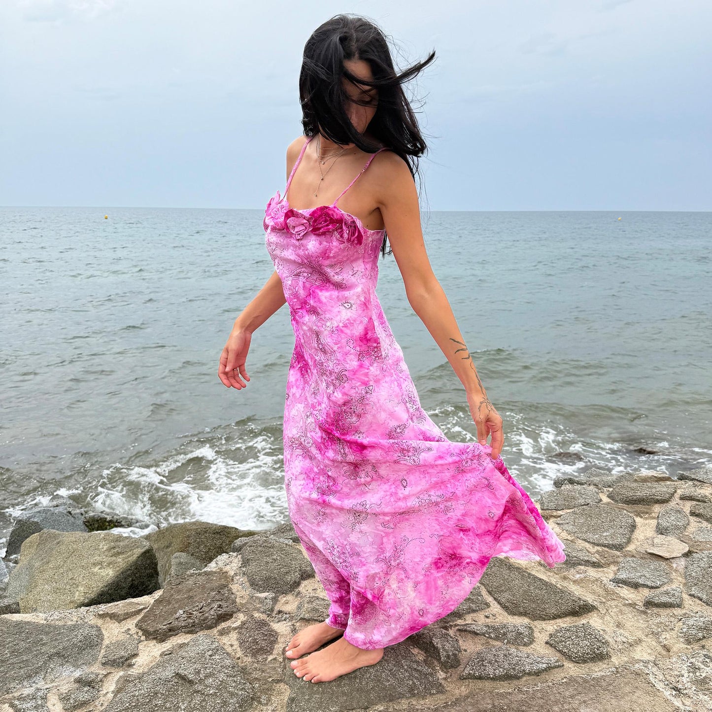 This vintage 2000s slip dress features a vivid pink tie-dye paisley print with rosette appliqué detail at the neckline. It flows into a long silhouette, ideal for summer weddings, proms, or formal parties, and comes with a matching scarf for versatile styling. A romantic archival piece made in France, perfect for bridal, evening, or statement occasions. Made from a non-stretch polyester blend. Excellent vintage condition.