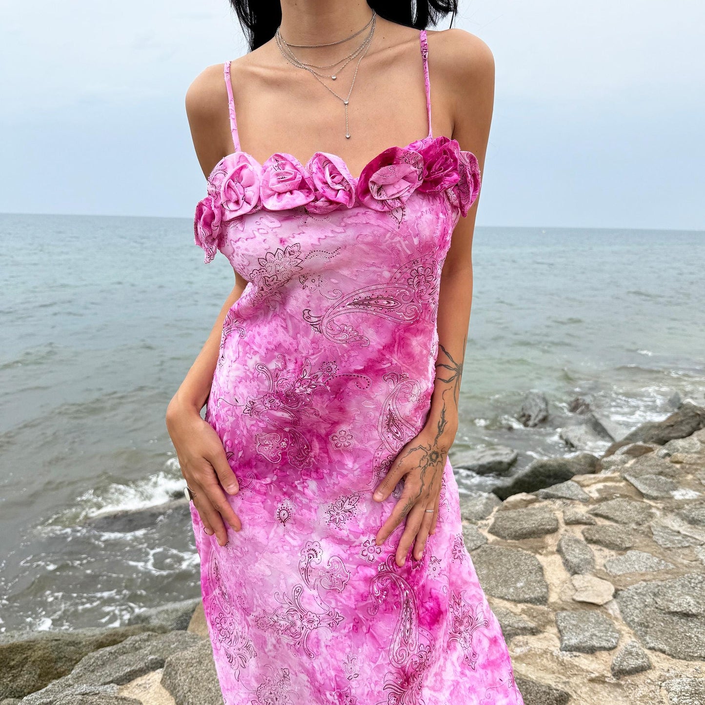 This vintage 2000s slip dress features a vivid pink tie-dye paisley print with rosette appliqué detail at the neckline. It flows into a long silhouette, ideal for summer weddings, proms, or formal parties, and comes with a matching scarf for versatile styling. A romantic archival piece made in France, perfect for bridal, evening, or statement occasions. Made from a non-stretch polyester blend. Excellent vintage condition.