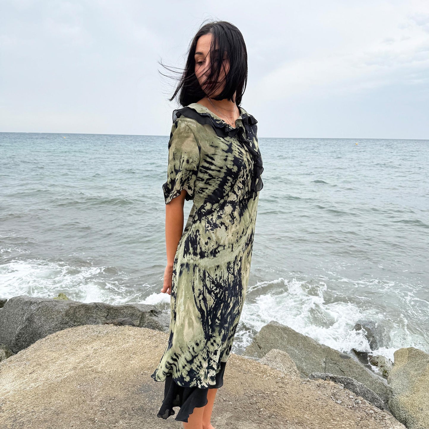 This vintage 90s midi dress features a black and green tie-dye pattern with a ruffled neckline. The short sleeves and flowy layered hem make it ideal for summer festivals, boho gatherings, or dark fairy-inspired looks. A unique Italian-made piece, perfect for forest parties or artistic styling. Made in Italy from lightweight non-stretch fabric. Excellent vintage condition.
