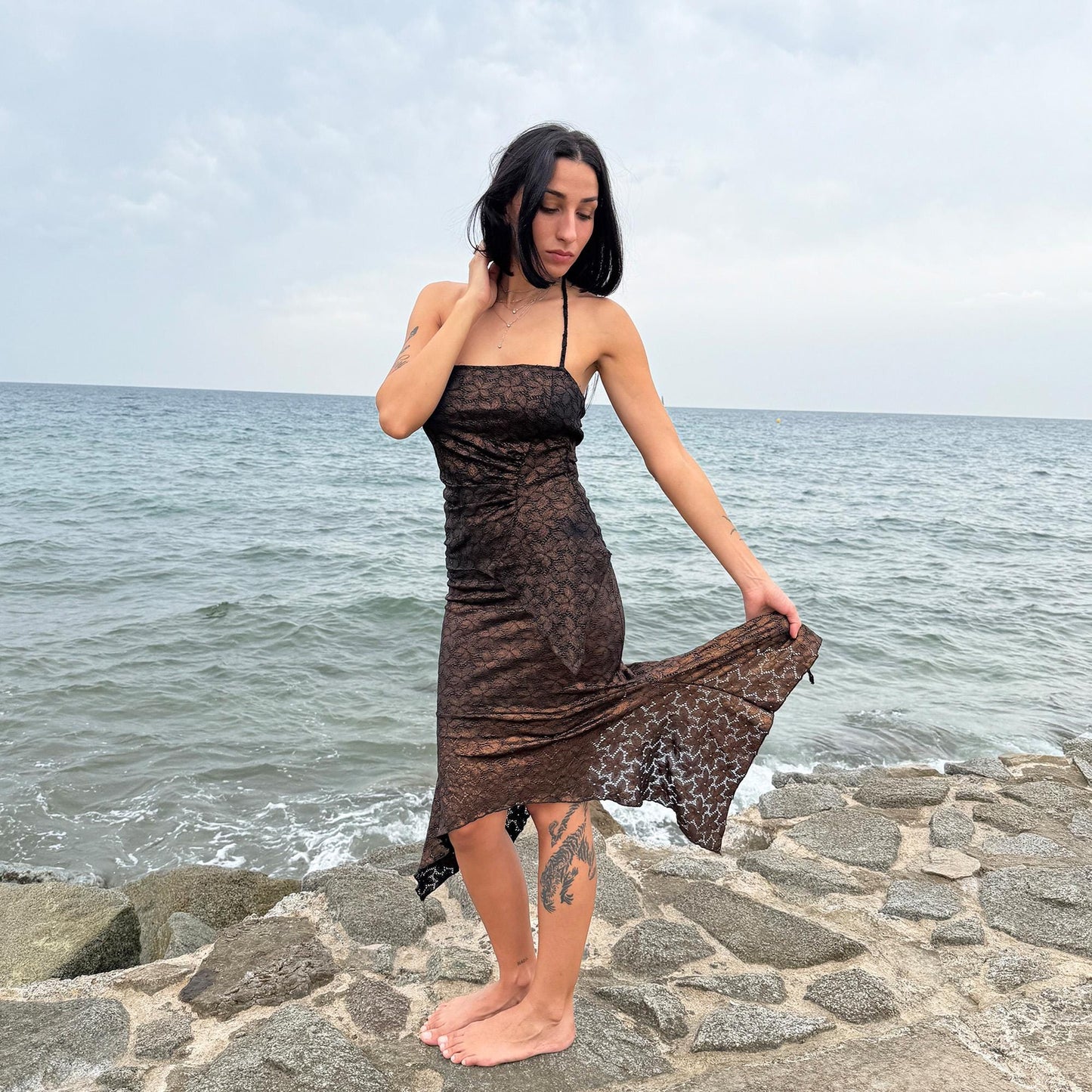 This vintage 2000s two-piece set features a shiny dark bronze-copper and black floral lace pattern. The handkerchief-style asymmetric midi skirt has an elastic waist and is paired with a matching ruched halter tie-neck top with an angled hem. A striking party set, perfect for festivals, summer nights, or dark whimsical styling. A rare archival coord for the ultimate fairy. Made in Spain from a stretchy polyester blend. Excellent vintage condition.