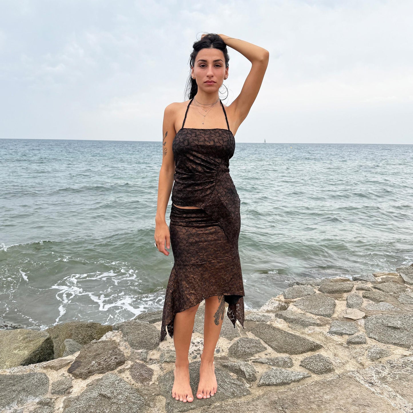 This vintage 2000s two-piece set features a shiny dark bronze-copper and black floral lace pattern. The handkerchief-style asymmetric midi skirt has an elastic waist and is paired with a matching ruched halter tie-neck top with an angled hem. A striking party set, perfect for festivals, summer nights, or dark whimsical styling. A rare archival coord for the ultimate fairy. Made in Spain from a stretchy polyester blend. Excellent vintage condition.