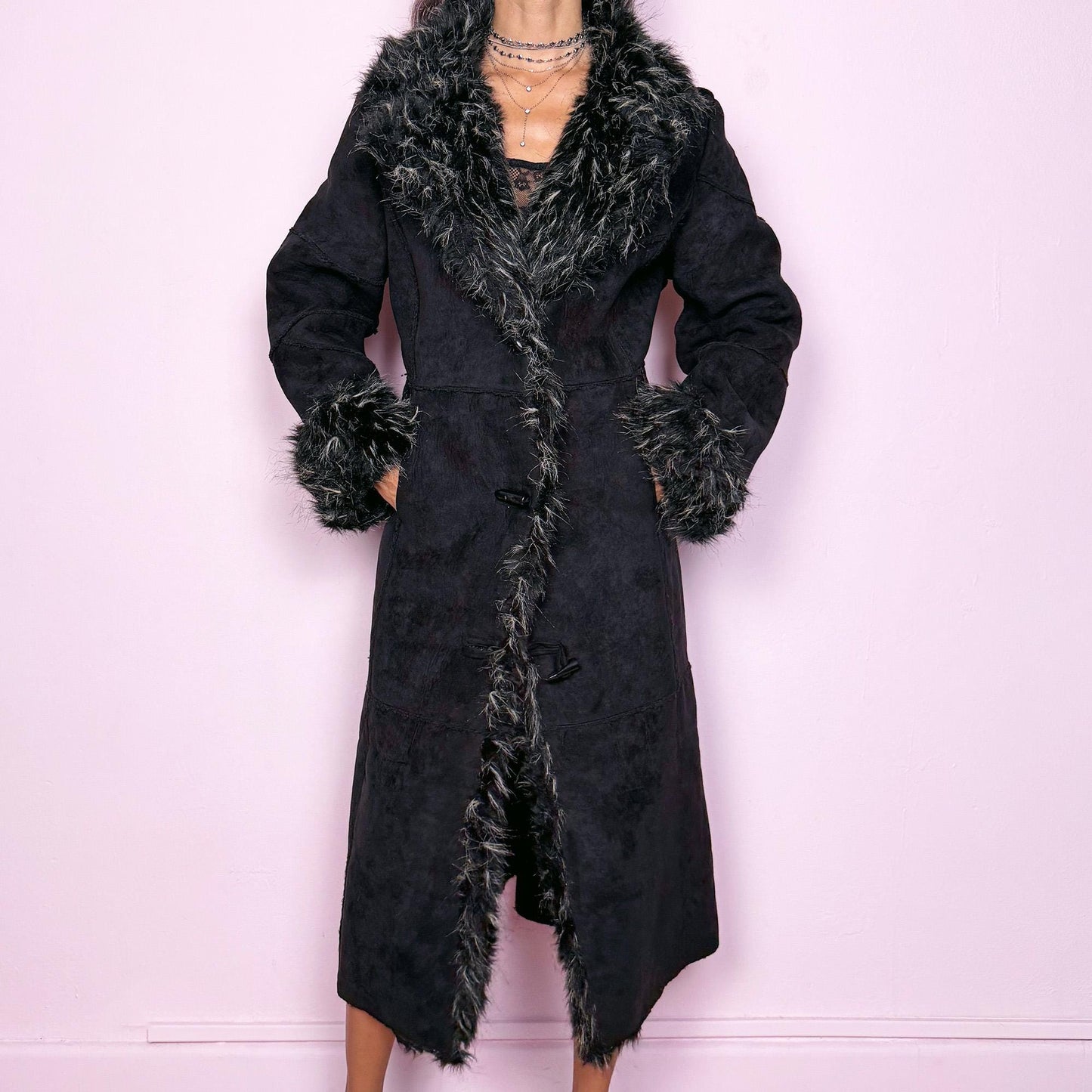 This vintage 2000s black maxi Penny Lane coat features a plush faux suede shell with dramatic black-and-beige faux fur trim at the collar and cuffs. Designed with toggle closures and side pockets, it offers warmth and structure while exuding bohemian gothic elegance. The long silhouette and textured fur detailing create a striking statement—perfect for winter nights, city wear, or whimsical Y2K layering. Made from polyester acrylic blend. Excellent vintage condition.