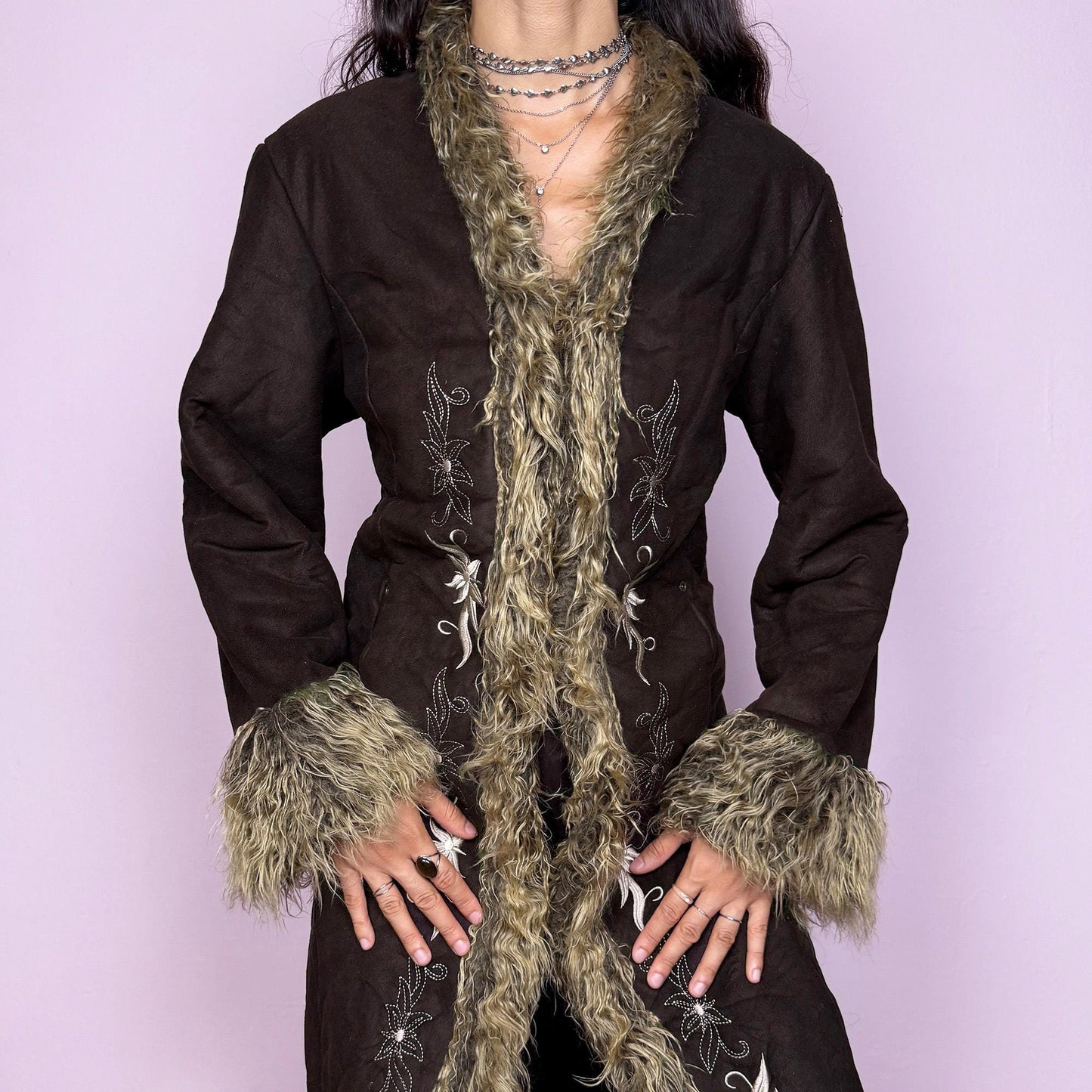 This vintage 2000s dark brown Penny Lane coat features beige faux fur trim at the collar, cuffs, and hem, with intricate floral embroidery along the front. Crafted from soft faux suede with pockets and dual snap-and-hook closure, it embodies the whimsical 70s Afghan-inspired Y2K aesthetic. Warm and romantic—perfect for fairycore, boho, and forest muse styling. Made from polyester faux suede and faux fur. Great vintage condition.