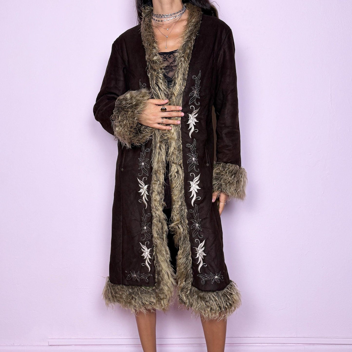 This vintage 2000s dark brown Penny Lane coat features beige faux fur trim at the collar, cuffs, and hem, with intricate floral embroidery along the front. Crafted from soft faux suede with pockets and dual snap-and-hook closure, it embodies the whimsical 70s Afghan-inspired Y2K aesthetic. Warm and romantic—perfect for fairycore, boho, and forest muse styling. Made from polyester faux suede and faux fur. Great vintage condition.