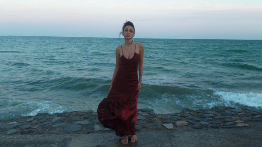 person in a long red satin dress standing by the sea in cinematic lighting, vintage aesthetic