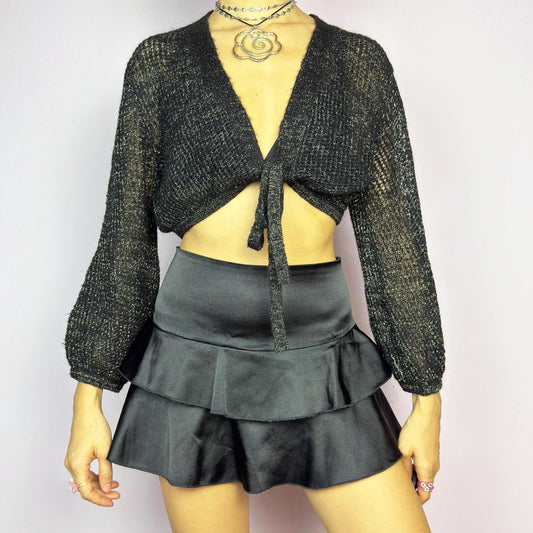 This Y2K Black Tie Front Cardigan is a vintage 2000s piece featuring a lightweight open-knit design with a subtle metallic shimmer, a cropped fit and long sleeves. Perfect for layering and ideal for night-out or casual outfits.