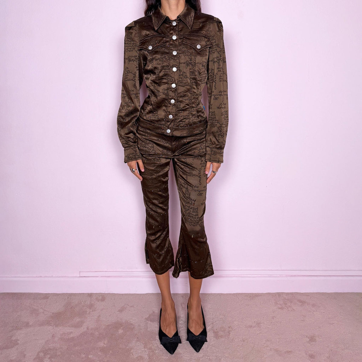 Vintage late 1990s two-piece set from French fashion house Christian Lacroix, from the Jeans de Christian Lacroix line, made in Italy. The set features a brown printed jacket with a glossy, satin-like finish, handwritten-style graphic motif, pointed collar, flap chest pockets, and branded snap-button closure, paired with matching high-waisted cropped trousers with a slim fit through the leg and flared hems. Crafted from a stretchy blend of acetate, polyamide, polyester, and elastane.