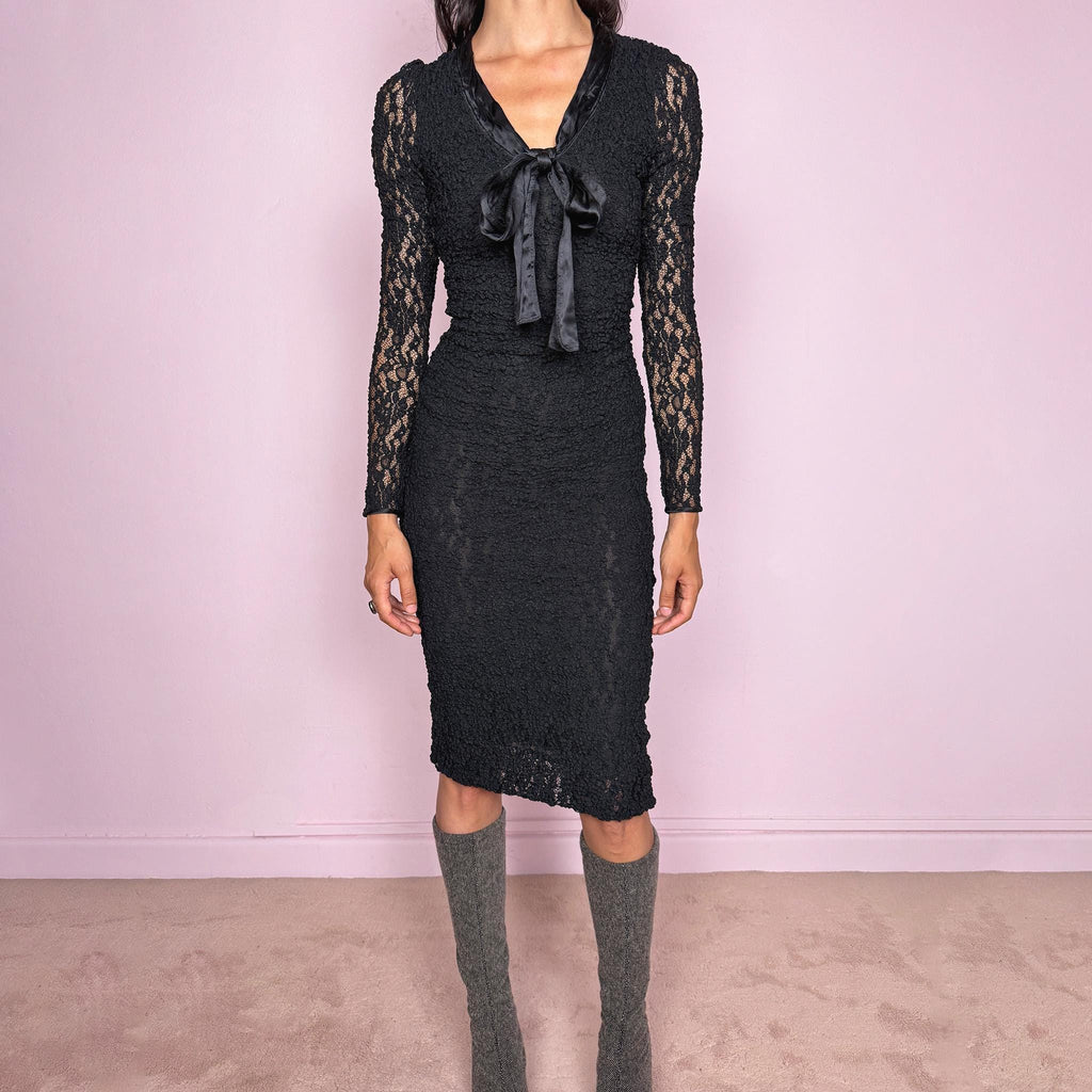 Vintage 2000s D&G Dolce & Gabbana black long sleeve midi dress crafted from stretchy silk-blend textured lace fabric. Fitted silhouette with sheer long sleeves, side zip closure, and satin bow tie detail at the neckline. A dark romantic designer piece with a sharp feminine silhouette, perfect for evening wear. Main fabric is polyamide and silk blend; lining is 93% silk and 7% elastane. Excellent vintage condition.