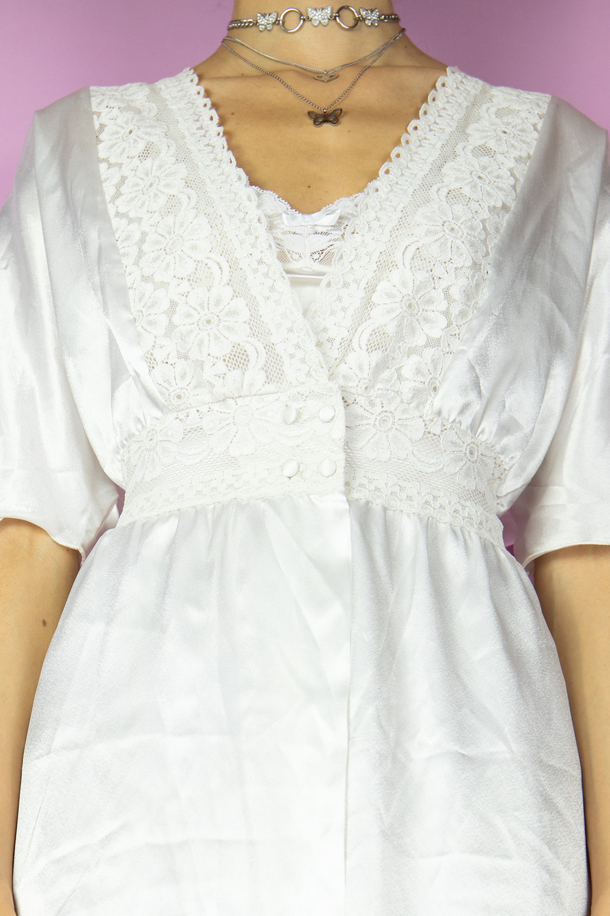 The Vintage 90s White Satin Duster Jacket is a white short-sleeved maxi duster coat with a button closure at the waist and lace details. Romantic 1990s white lace peignoir robe.