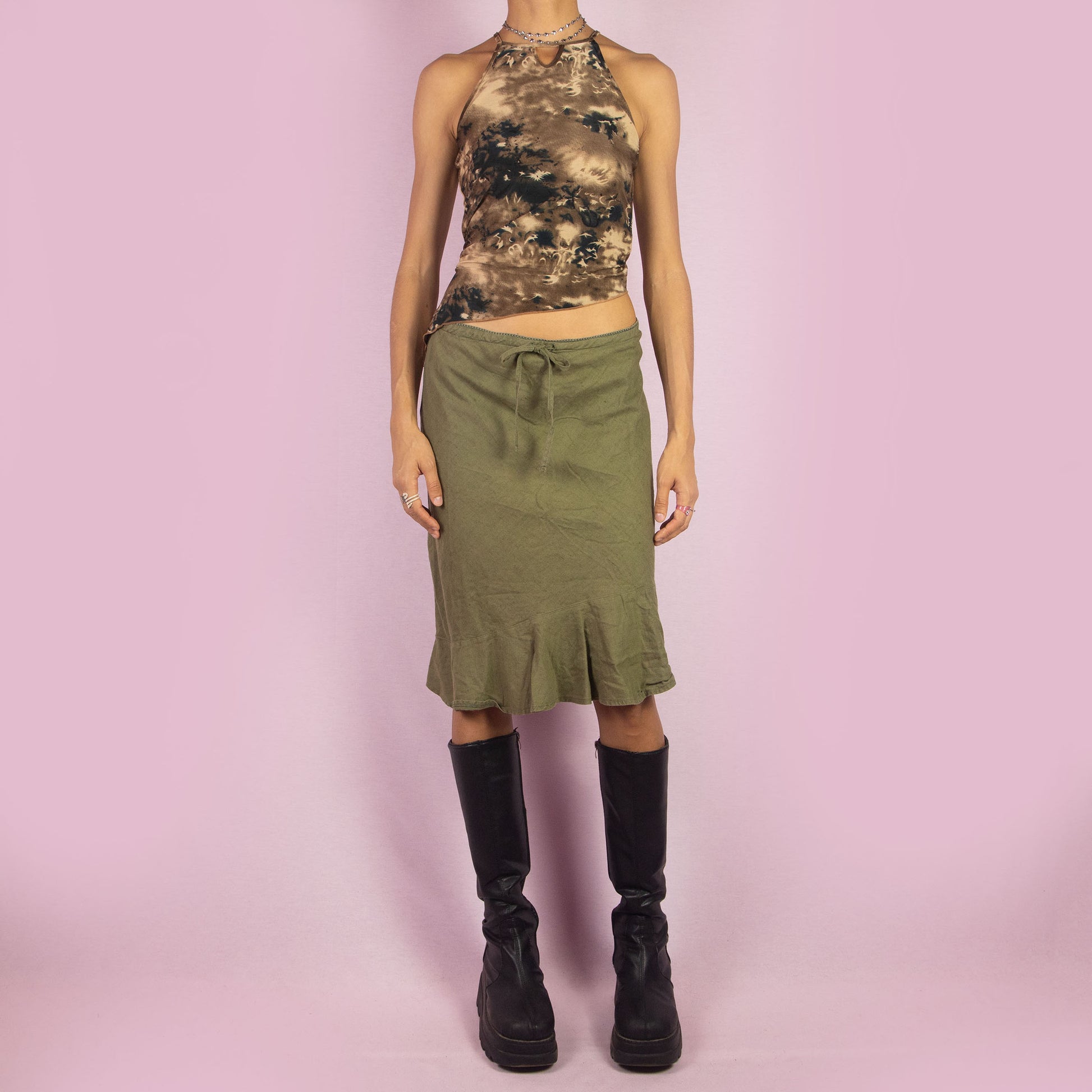 The Y2K Khaki Tie Waist Skirt is a vintage 2000s green mini skirt featuring a relaxed, high-waisted fit with a drawstring waist for adjustable styling. The skirt is finished with a subtle ruffle hem. Ideal for a casual summer look.