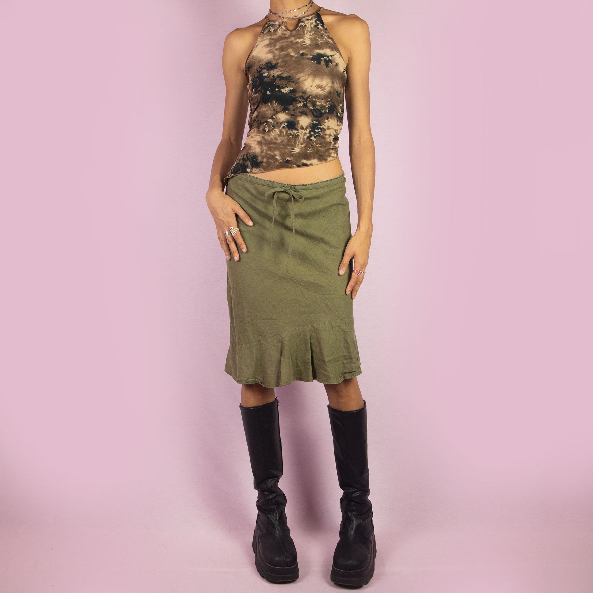 The Y2K Khaki Tie Waist Skirt is a vintage 2000s green mini skirt featuring a relaxed, high-waisted fit with a drawstring waist for adjustable styling. The skirt is finished with a subtle ruffle hem. Ideal for a casual summer look.