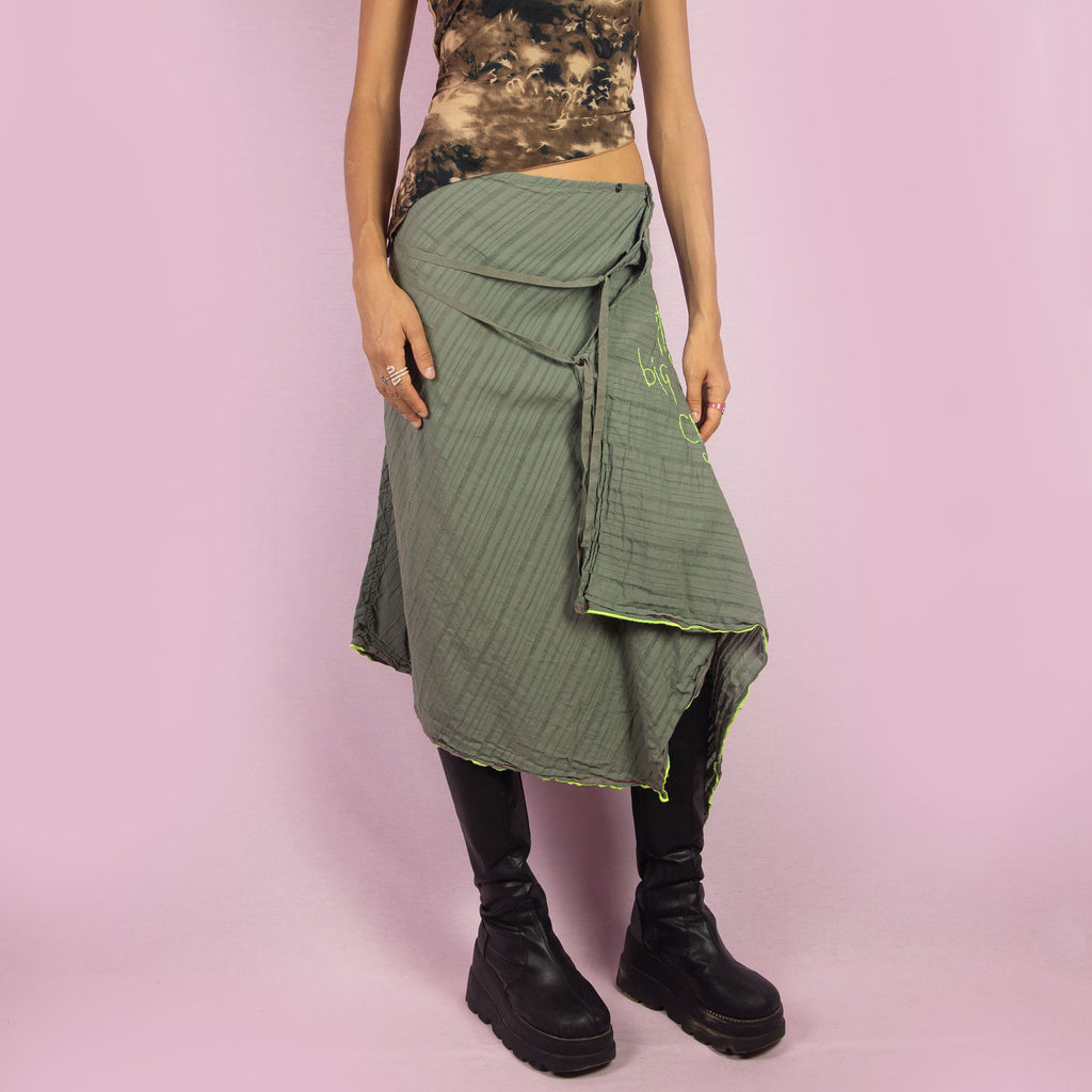 The Y2K Khaki Asymmetric Cop Copine Skirt is a unique vintage 2000s midi skirt showcasing the brand's signature avant-garde style. This high-waisted skirt features an asymmetrical hem and snap button detailing. Made with a lightweight fabric, it's an ideal choice for summer.