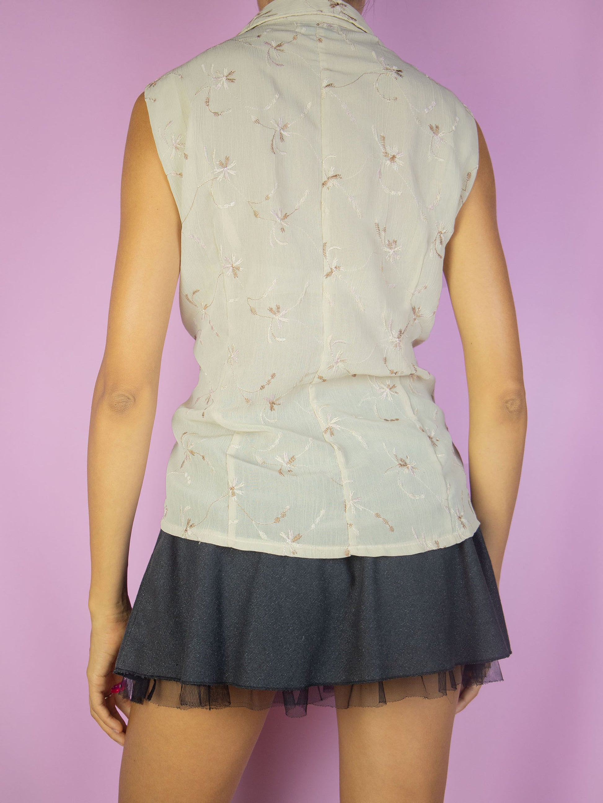 The Vintage 90s Boho Beige Sleeveless Blouse is a summer shirt with light brown embroidered floral details, a collar and buttons.