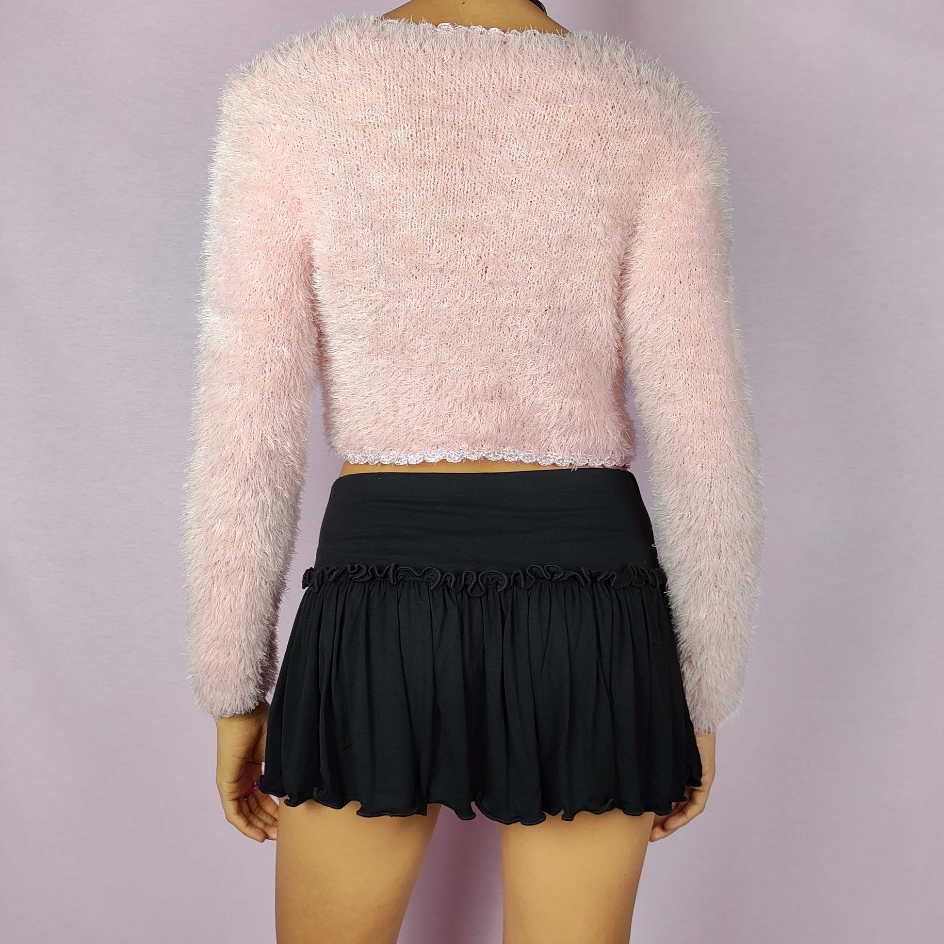 The Vintage 90s Pink Cropped Cardigan is a cozy, fuzzy knit piece that adds a soft and romantic touch to any outfit. This delicate cardigan features a cropped silhouette, a button closure and a fluffy texture in a pastel pink shade. Ideal for a cute and comfy look.