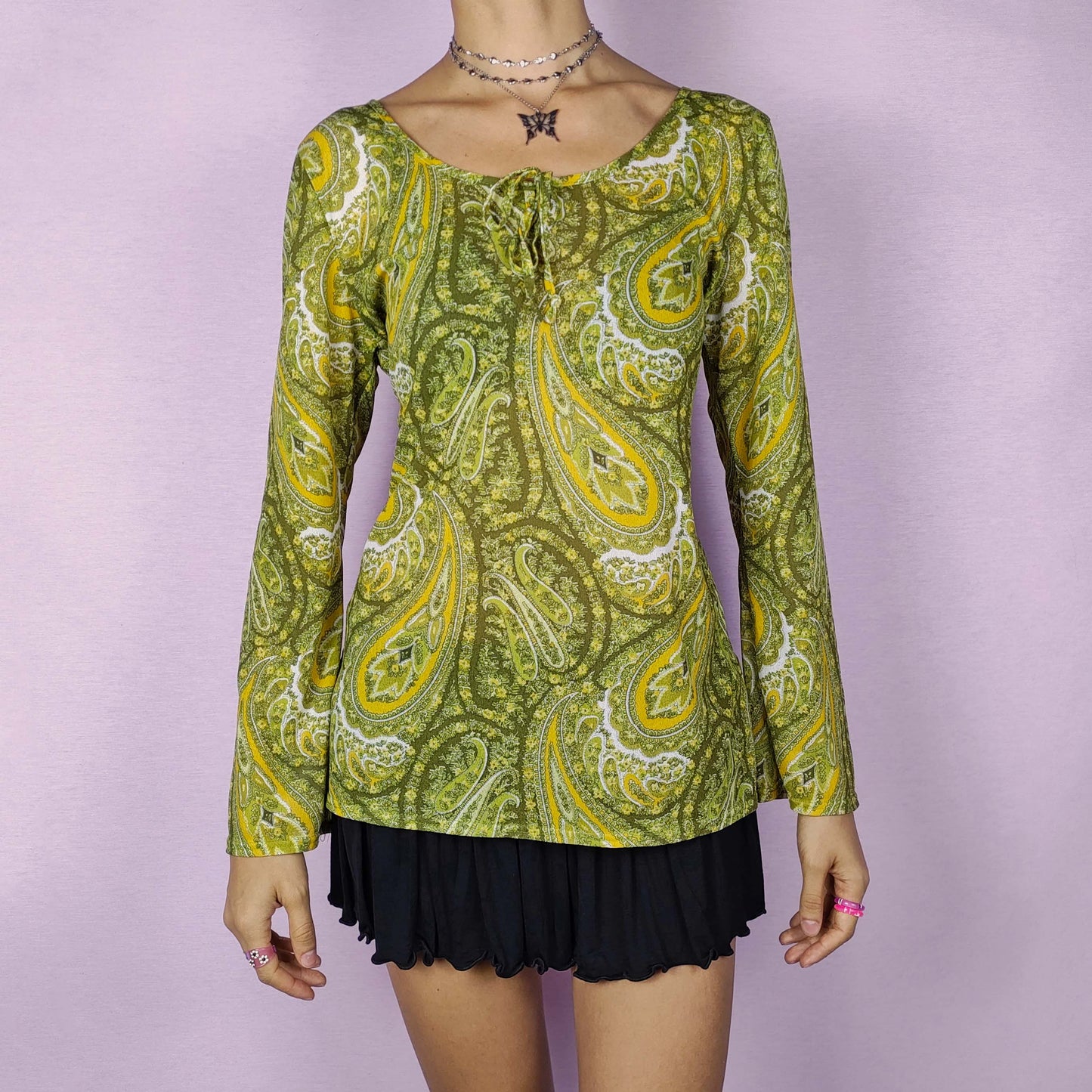The Y2K Mesh Tie Front Top is a vintage 2000s semi-sheer blouse with a vibrant green and yellow paisley floral print. This lightweight and stretchy mesh top features a tie detail at the neckline and flared bell sleeves for a boho-chic vibe. Perfect for summer casual outfits.