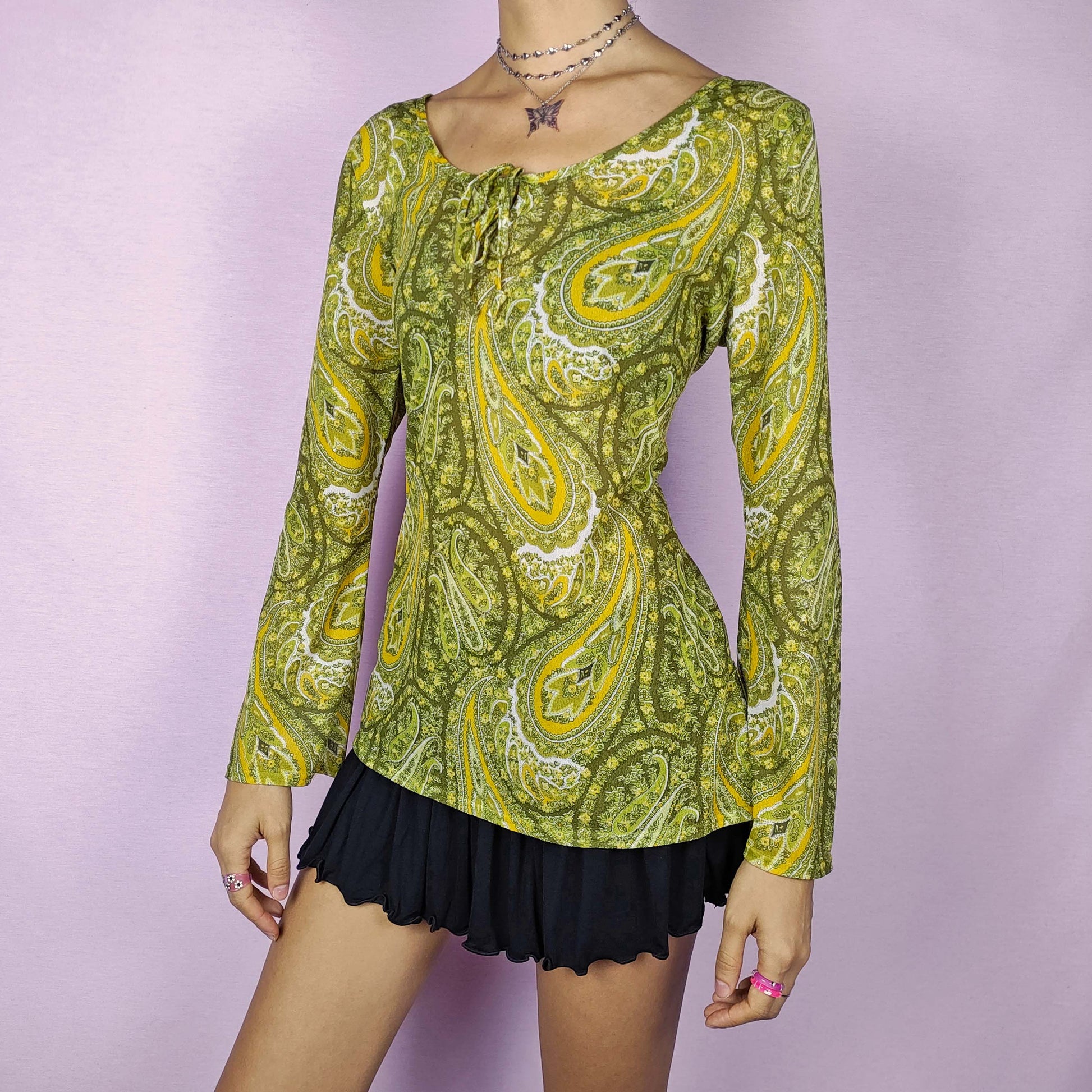 The Y2K Mesh Tie Front Top is a vintage 2000s semi-sheer blouse with a vibrant green and yellow paisley floral print. This lightweight and stretchy mesh top features a tie detail at the neckline and flared bell sleeves for a boho-chic vibe. Perfect for summer casual outfits.