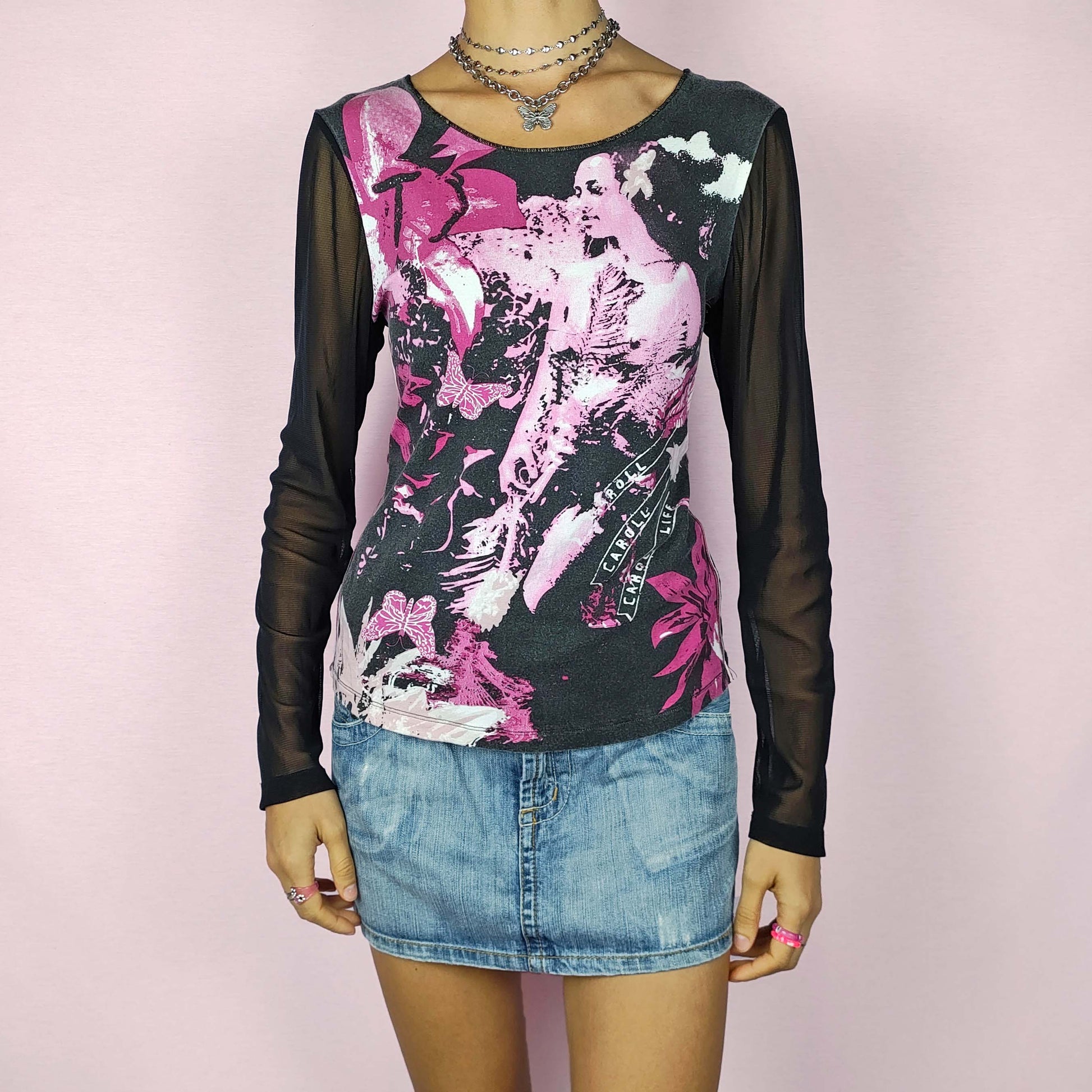 The Y2K Black Print Mesh Top is a vintage 2000s stretchy piece featuring a pink and white graphic print across the front and sheer black mesh long sleeves. Perfect for casual wear or dressing up for a night out.