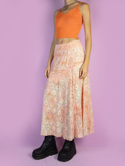 The Vintage 90s Fairy Lace Midi Skirt is a pastel light orange and beige floral-patterned mesh maxi skirt adorned with glitter and ruffle details, featuring a side zipper closure. Flowy and romantic, it's perfect for summer evenings and party occasions. Made in Spain.