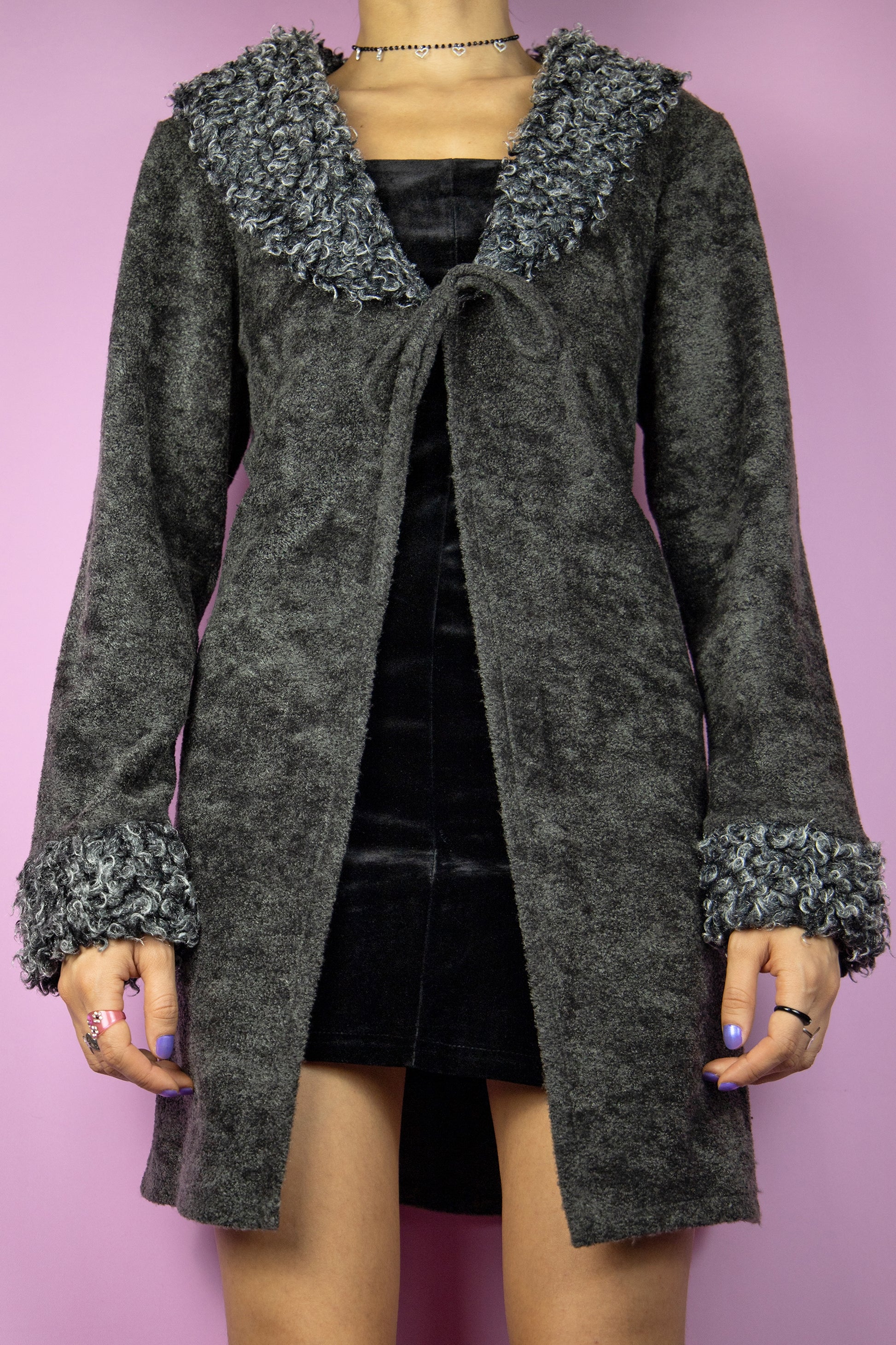 The Y2K Gray Faux Fur Duster Jacket is a vintage 2000s piece inspired by the iconic Penny Lane style, featuring a cozy textured fabric in a deep charcoal gray, an open-front design with a tie closure and a faux fur trim along the collar and cuffs, adding a touch of whimsy. Perfect for evening parties and formal occasions.
