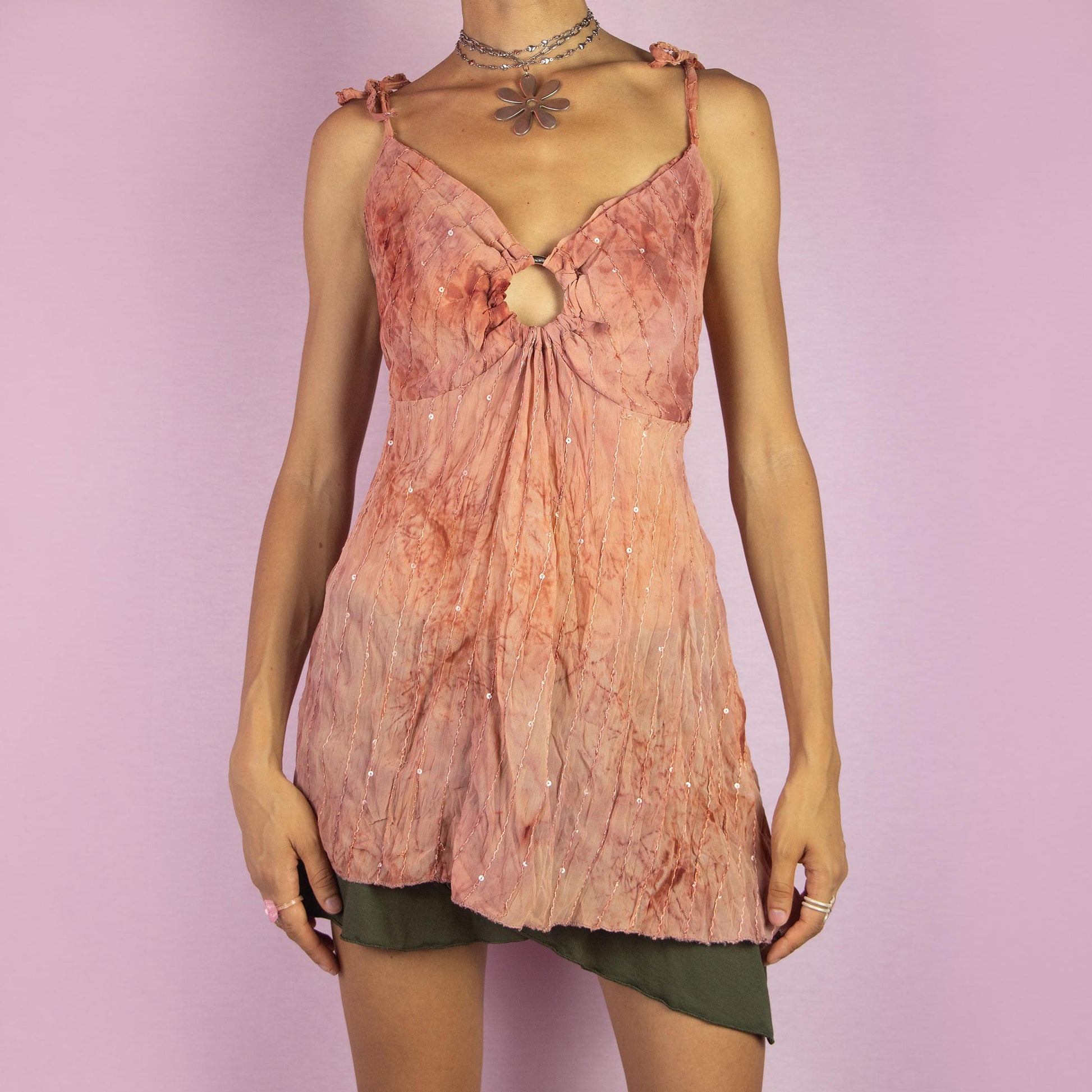 The Y2K Tie Dye Flowy Top is a vintage 2000s boho-inspired piece featuring a soft terracotta tie-dye pattern, delicate sequin embellishments, and a flattering keyhole front detail. Designed with adjustable shoulder ties and a flowing silhouette, it also features an asymmetrical pointed hem, making it perfect for summer festivals or relaxed casual outings.