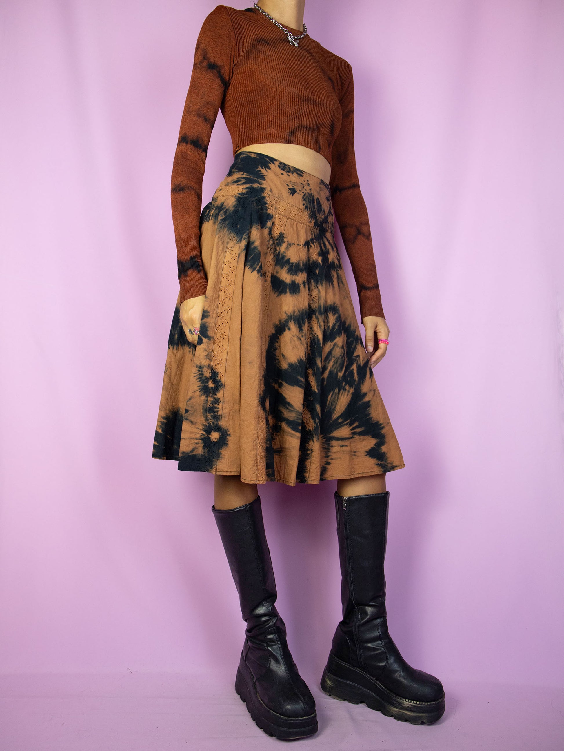 The Vintage 90s Tie Dye Midi Skirt is a statement piece featuring a tie-dye pattern in brown and black, a high-waisted fit with eyelet details and a side zipper closure. Perfect for festival wear or summer outings.