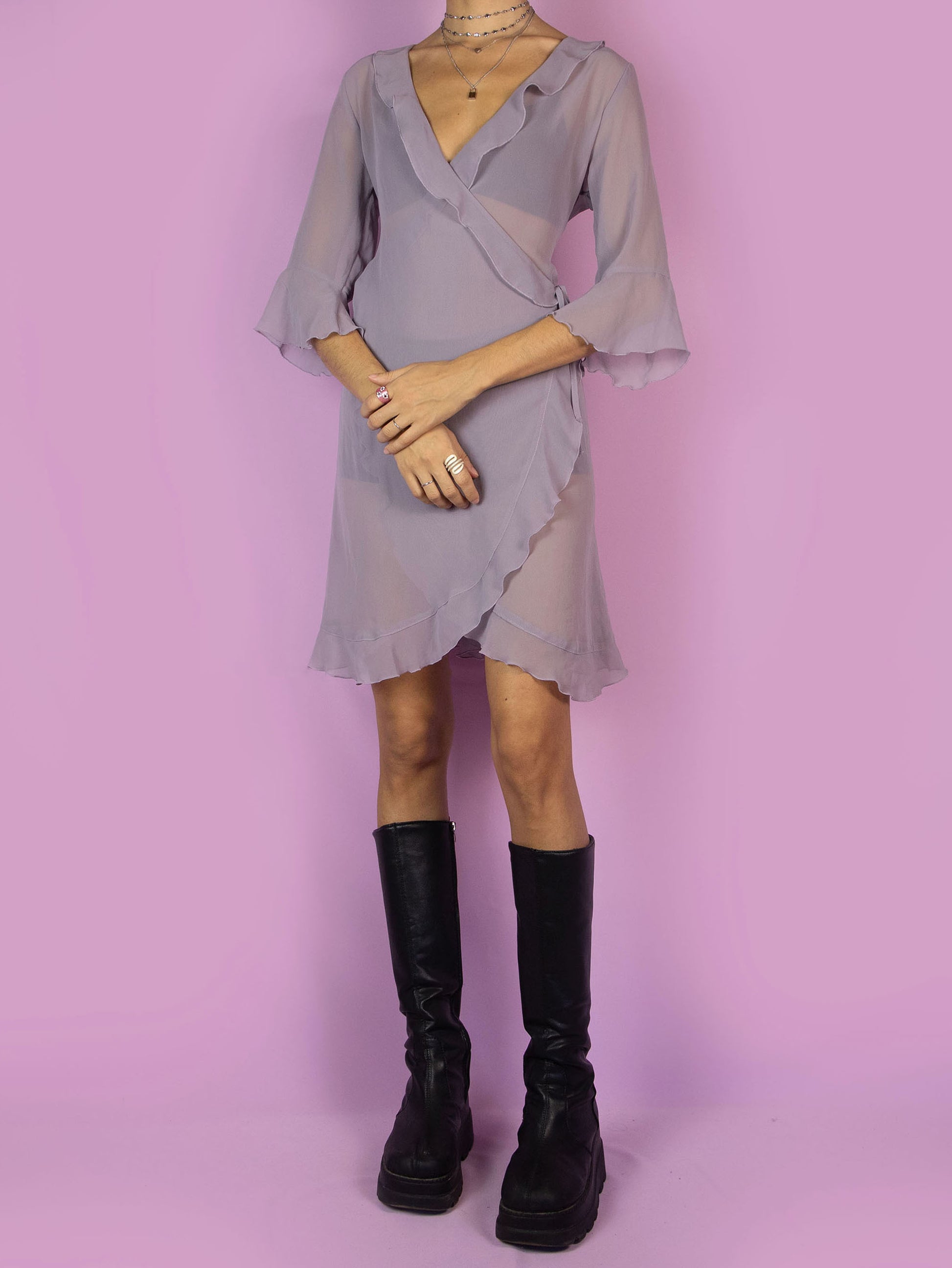 The Y2K Purple Wrap Dress is a vintage 2000s dreamy and romantic piece featuring a soft sheer fabric in a muted lavender shade. Designed with a deep V-neckline, ruffled trim, and flared 3/4 sleeves, this dress wraps around and ties at the side for an adjustable fit. Perfect for springtime outings, date nights, or festival-inspired looks.